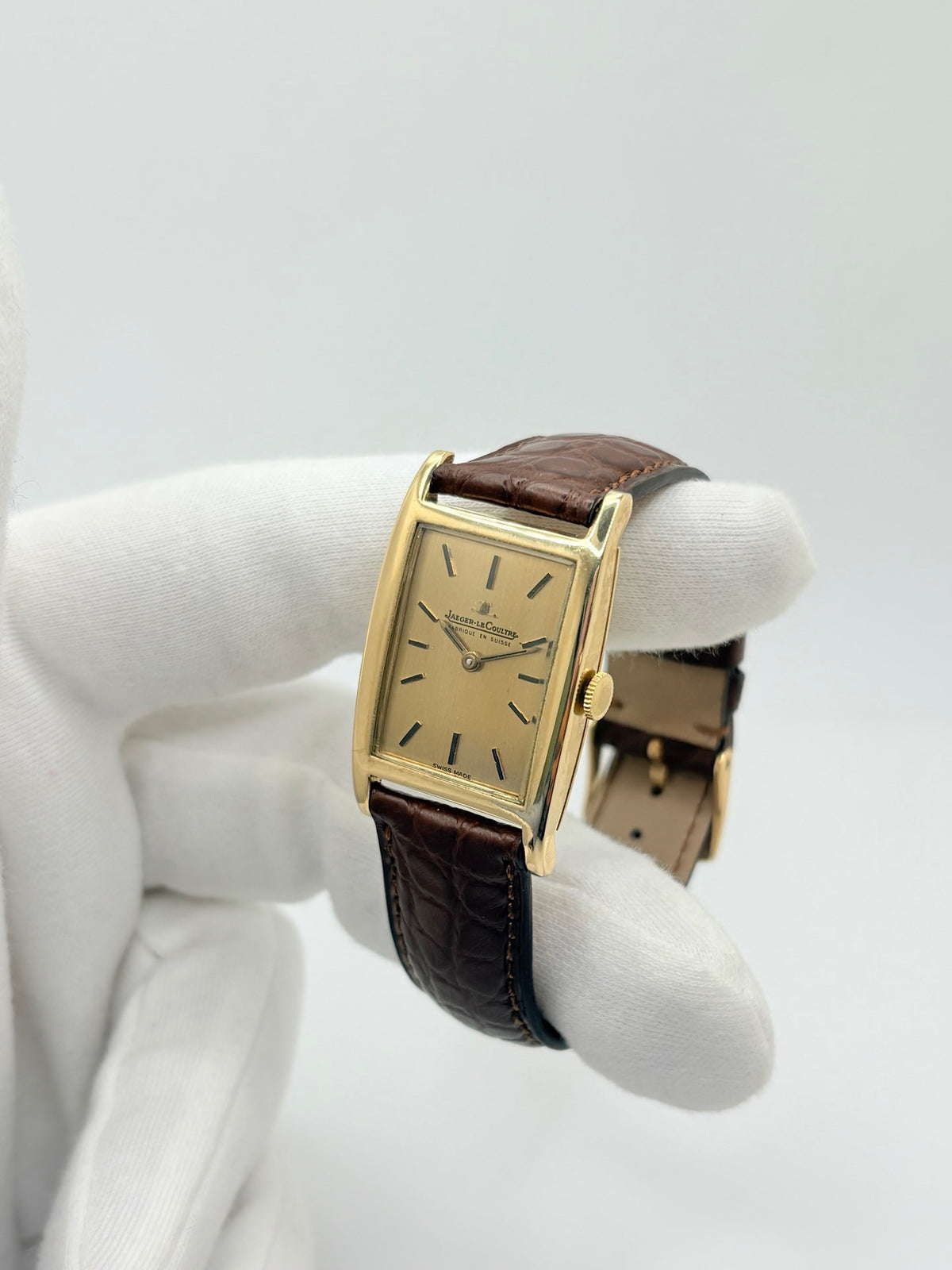 Montre Jaeger-LeCoultre Classic 9012 vintage à remontage manuel, datant approximativement de 1960. Son boîtier rectangulaire en or jaune de 37 × 23 mm est équipé d’un verre Plexiglas et d’un élégant cadran or à index bâtons. Cette montre Jaeger-LeCoultre est montée sur un bracelet brun en cuir de crocodile avec boucle ardillon en acier. En très bon état, elle présente de légères traces d’usure et est proposée avec son coffret d’origine.
