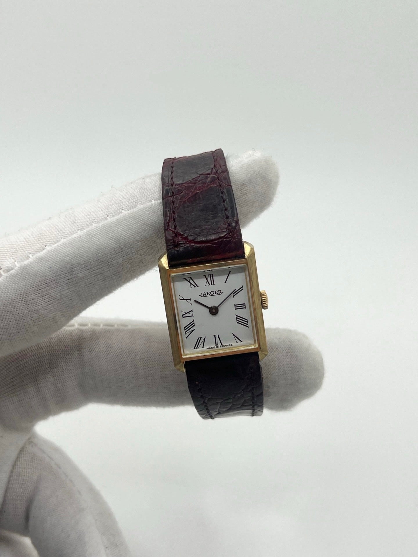 Montre vintage classique en or jaune 18 carats avec boîtier rond de 20 mm, mouvement mécanique à remontage manuel et cadran blanc à chiffres romains. Montre élégante au style intemporel, dotée d’un verre minéral et d’un bracelet en cuir bordeaux avec boucle déployante en acier. Modèle ancien révisé, en très bon état, idéal pour les amateurs de montres de collection et d’horlogerie traditionnelle.