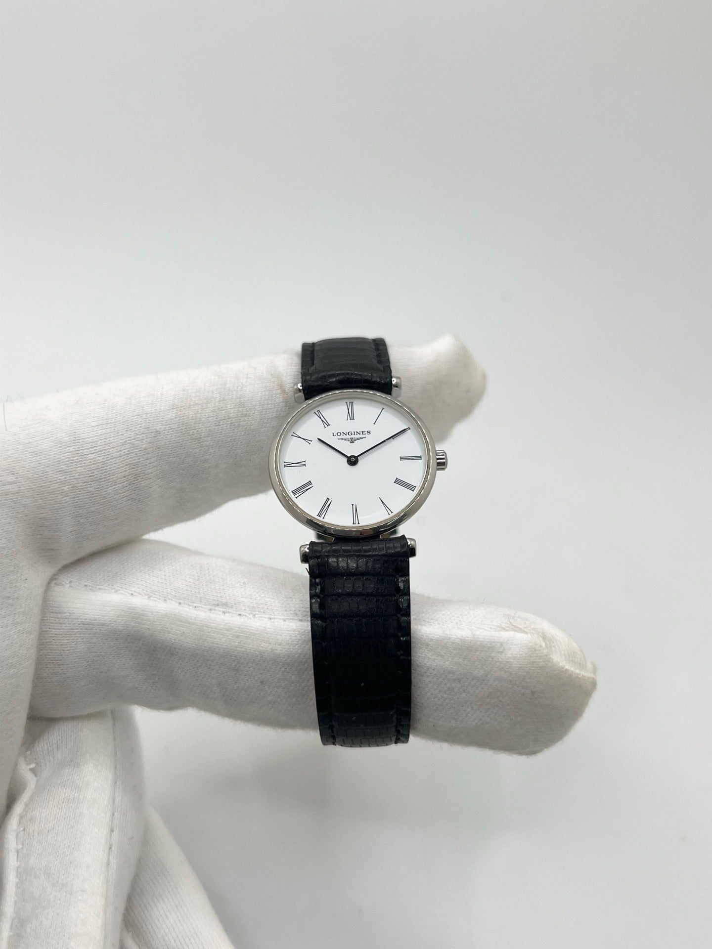 Montre Longines La Grande Classique L4.209.4 pour femme en acier avec bracelet en cuir de lézard noir. Ce modèle à mouvement quartz est doté d'un boîtier de 24 mm, d'un cadran blanc épuré sans chiffres, d'une lunette en acier et d'un verre saphir. Élégante et intemporelle, cette montre de luxe d'occasion est en très bon état avec de légères traces d'usure. Son design raffiné en fait un choix idéal pour un usage quotidien ou une collection horlogère.