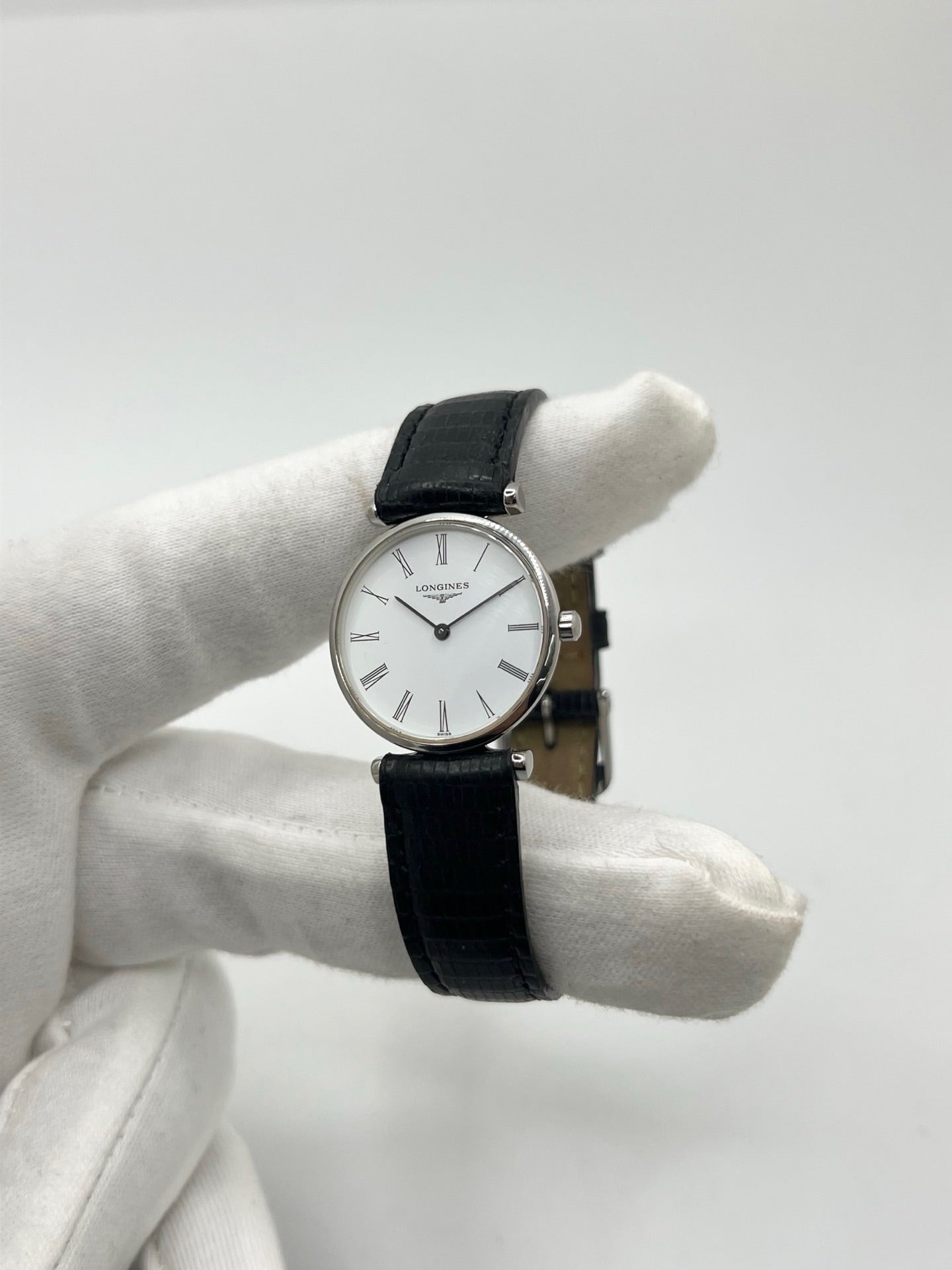 Montre Longines La Grande Classique L4.209.4 pour femme en acier avec bracelet en cuir de lézard noir. Ce modèle à mouvement quartz est doté d'un boîtier de 24 mm, d'un cadran blanc épuré sans chiffres, d'une lunette en acier et d'un verre saphir. Élégante et intemporelle, cette montre de luxe d'occasion est en très bon état avec de légères traces d'usure. Son design raffiné en fait un choix idéal pour un usage quotidien ou une collection horlogère.