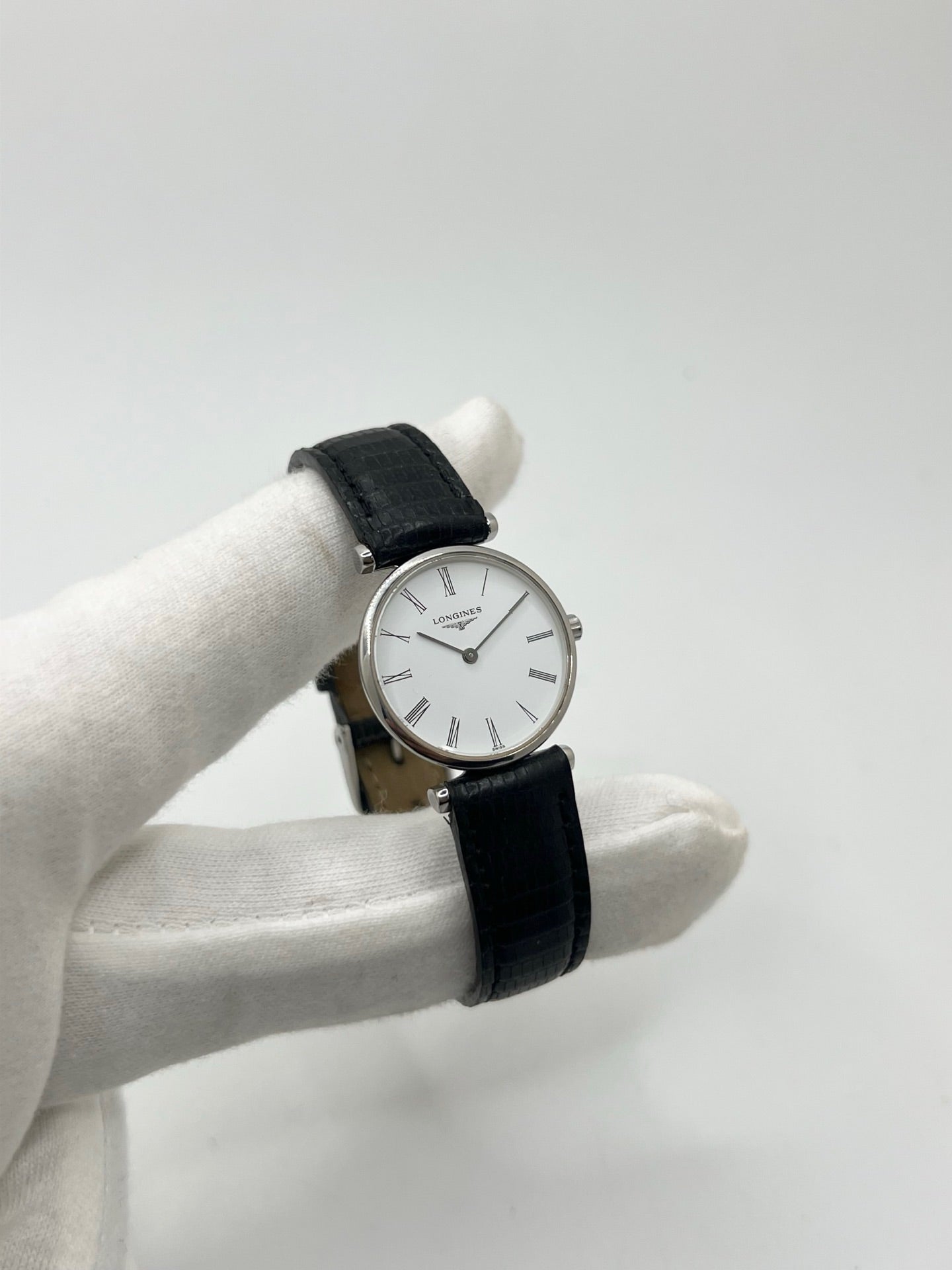 Montre Longines La Grande Classique L4.209.4 pour femme en acier avec bracelet en cuir de lézard noir. Ce modèle à mouvement quartz est doté d'un boîtier de 24 mm, d'un cadran blanc épuré sans chiffres, d'une lunette en acier et d'un verre saphir. Élégante et intemporelle, cette montre de luxe d'occasion est en très bon état avec de légères traces d'usure. Son design raffiné en fait un choix idéal pour un usage quotidien ou une collection horlogère.