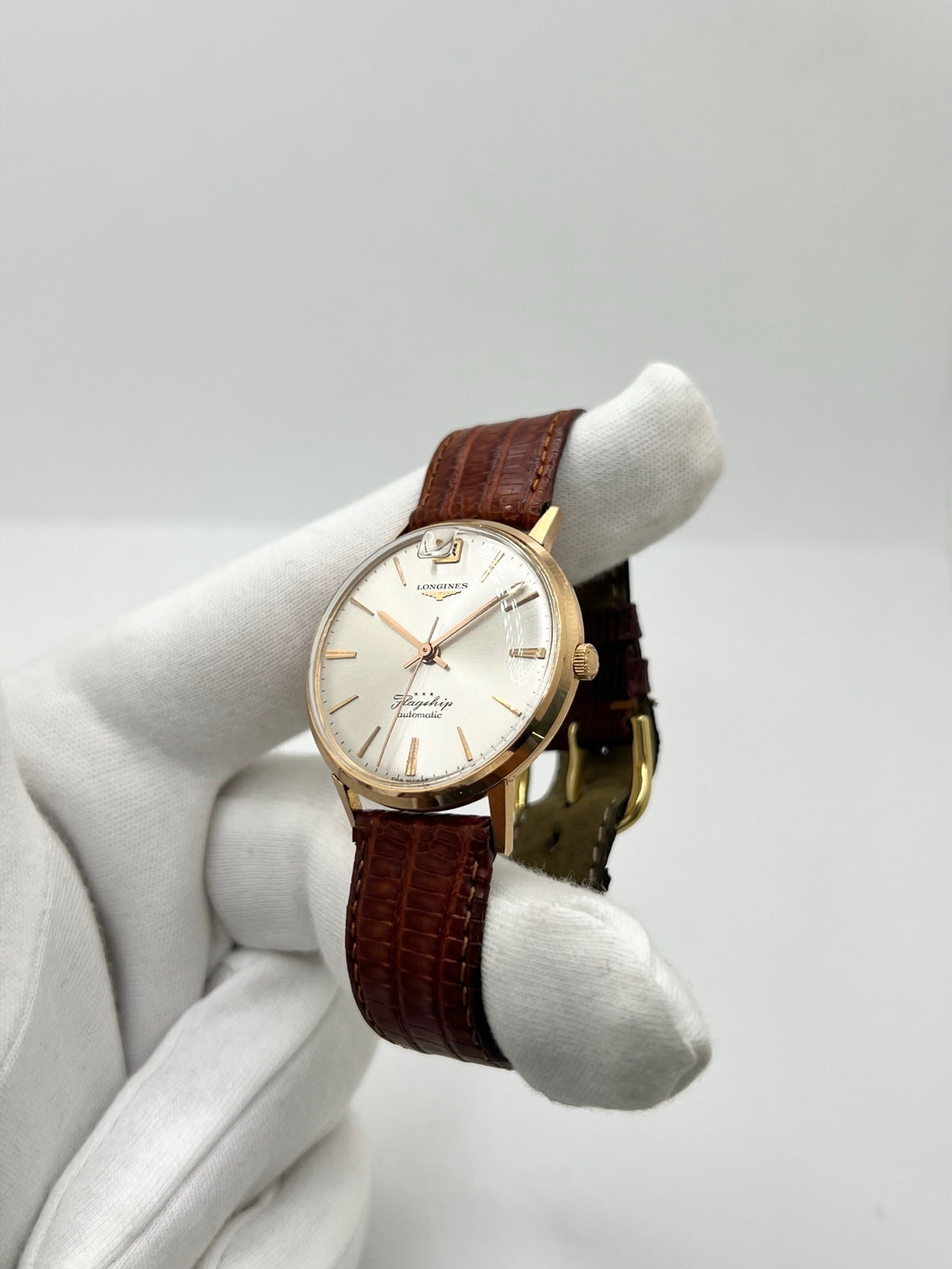 Montre Longines Flagship 2407 vintage en très bon état, datant approximativement de 1962, avec mouvement automatique calibre 341. Son boîtier de 35 mm en or rose est associé à un cadran argent à index bâtons et un verre Plexiglas. Cette Longines Flagship possède un bracelet en cuir de lézard brun avec boucle ardillon en acier. Elle dispose également d’une fonction date et d’un design élégant et intemporel.