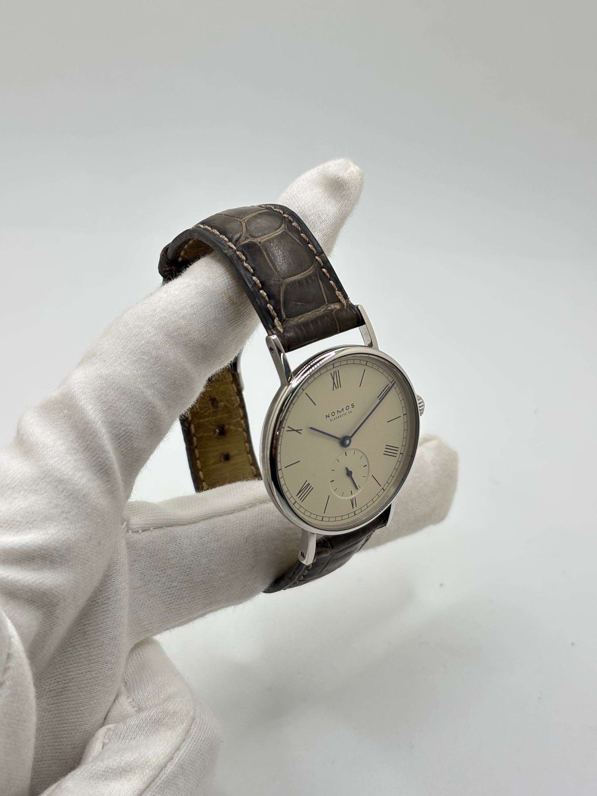 Montre Nomos Glashütte Ludwig 205 en acier avec boîtier de 37,5 mm, mouvement à remontage manuel offrant 43 heures de réserve de marche et cadran blanc à chiffres romains. Équipée d'un verre saphir, d'un bracelet en cuir noir, d'une petite seconde, d'un fond transparent et d'aiguilles en acier bleui, cette montre de luxe d'occasion est en très bon état avec de légères traces d'usure. Un modèle élégant au style intemporel, idéal pour les amateurs d'horlogerie.
