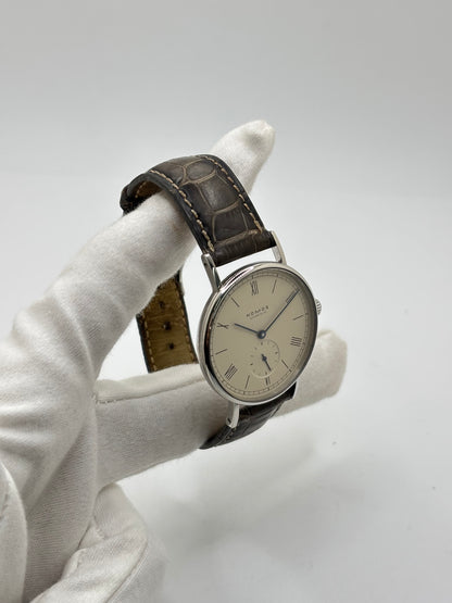 Montre Nomos Glashütte Ludwig 205 en acier avec boîtier de 37,5 mm, mouvement à remontage manuel offrant 43 heures de réserve de marche et cadran blanc à chiffres romains. Équipée d'un verre saphir, d'un bracelet en cuir noir, d'une petite seconde, d'un fond transparent et d'aiguilles en acier bleui, cette montre de luxe d'occasion est en très bon état avec de légères traces d'usure. Un modèle élégant au style intemporel, idéal pour les amateurs d'horlogerie.
