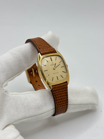 Montre Omega De Ville vintage référence 511.0531 en plaqué or datant de 1969, équipée d'un mouvement à remontage manuel. Son cadran doré à index bâtons est protégé par un verre en matière plastique. Son boîtier de 25 mm est associé à un bracelet en cuir brun avec boucle ardillon en acier. Cette montre d'occasion, révisée et en très bon état, séduit par son élégance intemporelle et son style classique des années 1960.