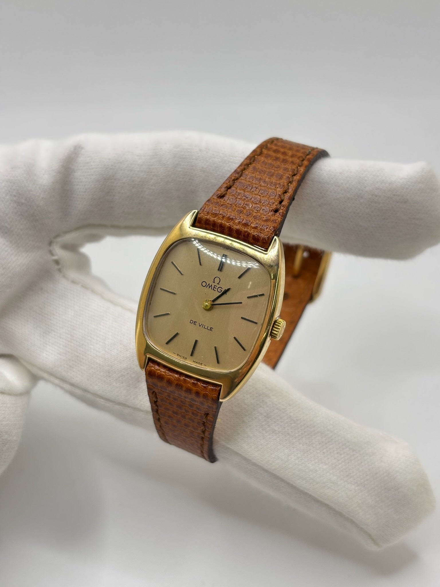 Montre Omega De Ville vintage référence 511.0531 en plaqué or datant de 1969, équipée d'un mouvement à remontage manuel. Son cadran doré à index bâtons est protégé par un verre en matière plastique. Son boîtier de 25 mm est associé à un bracelet en cuir brun avec boucle ardillon en acier. Cette montre d'occasion, révisée et en très bon état, séduit par son élégance intemporelle et son style classique des années 1960.