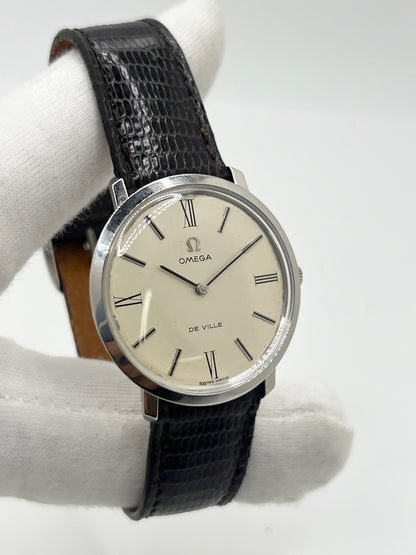 Montre Omega De Ville vintage référence 111.077 en acier, fabriquée en 1969. Ce modèle à remontage manuel est doté d'un cadran argent avec chiffres romains, d'un verre en plexiglas et d'un boîtier de 33 mm. Le bracelet en cuir noir avec boucle ardillon en acier complète son style classique et intemporel. Cette montre d'occasion révisée séduit les amateurs d'horlogerie vintage et de montres Omega de collection.
