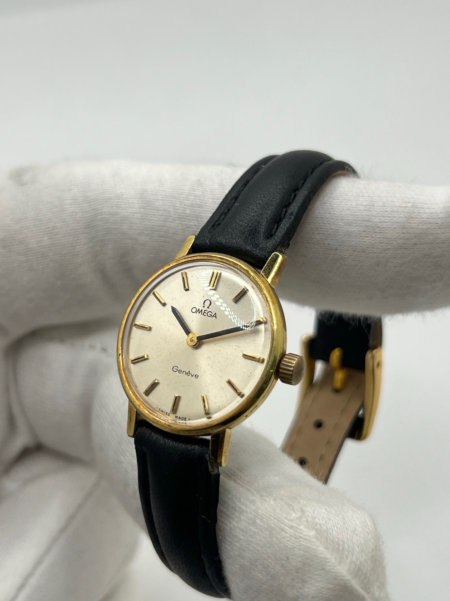 Montre Omega Genève femme vintage de 1972 en plaqué or, avec mouvement à remontage manuel. Boîtier de 23 mm au cadran doré orné de pierres précieuses et verre en plastique. Bracelet en cuir noir avec boucle en acier. Modèle élégant et intemporel, en bon état avec traces d’usure visibles. Révisée en avril 2026, vendue sans coffret ni papiers, disponible en stock en France.