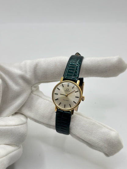 Montre Omega Genève vintage référence 511.0457 pour femme, fabriquée vers 1972 et équipée d'un mouvement à remontage manuel. Son boîtier en acier de 23 mm est associé à un cadran blanc à index bâtons protégé par un verre en matière plastique. Elle est montée sur un bracelet en cuir vert avec boucle ardillon en acier. Révisée en interne et proposée en très bon état, cette montre d'occasion incarne l'élégance discrète et le savoir-faire horloger suisse des années 1970.