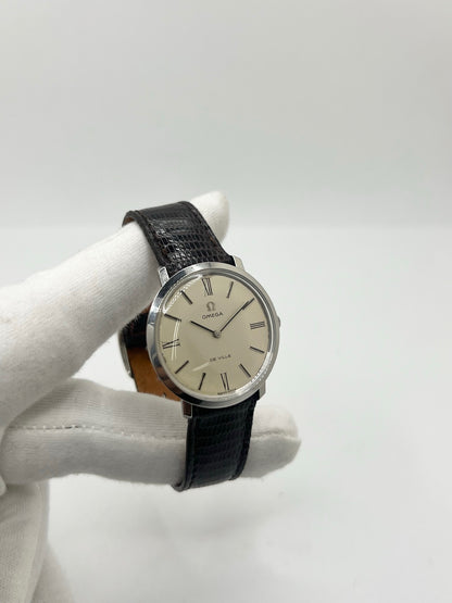 Montre Omega De Ville vintage référence 111.077 en acier, fabriquée en 1969. Ce modèle à remontage manuel est doté d'un cadran argent avec chiffres romains, d'un verre en plexiglas et d'un boîtier de 33 mm. Le bracelet en cuir noir avec boucle ardillon en acier complète son style classique et intemporel. Cette montre d'occasion révisée séduit les amateurs d'horlogerie vintage et de montres Omega de collection.
