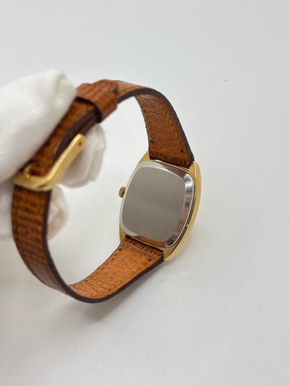Montre Omega De Ville vintage référence 511.0531 en plaqué or datant de 1969, équipée d'un mouvement à remontage manuel. Son cadran doré à index bâtons est protégé par un verre en matière plastique. Son boîtier de 25 mm est associé à un bracelet en cuir brun avec boucle ardillon en acier. Cette montre d'occasion, révisée et en très bon état, séduit par son élégance intemporelle et son style classique des années 1960.