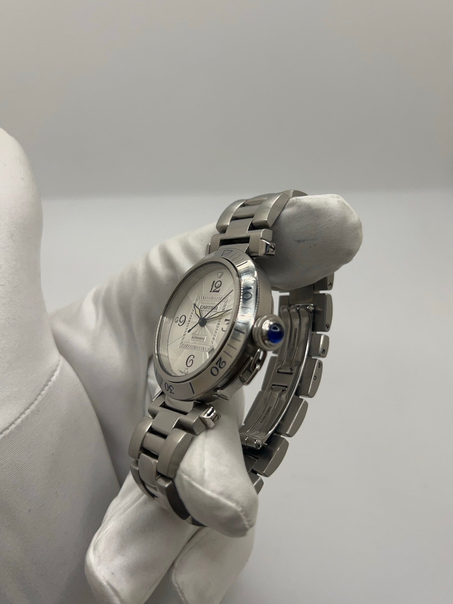 Montre Cartier Pasha automatique en acier, boîtier 38 mm avec verre saphir et cadran argent à chiffres arabes. Équipée d’un mouvement automatique calibre Cartier 191 avec fonction date. Bracelet acier avec boucle déployante. Modèle d’occasion en très bon état, révisé, présentant de légères micro-rayures peu visibles. Montre élégante et sportive, adaptée à un usage quotidien, livrée avec son coffret d’origine.
