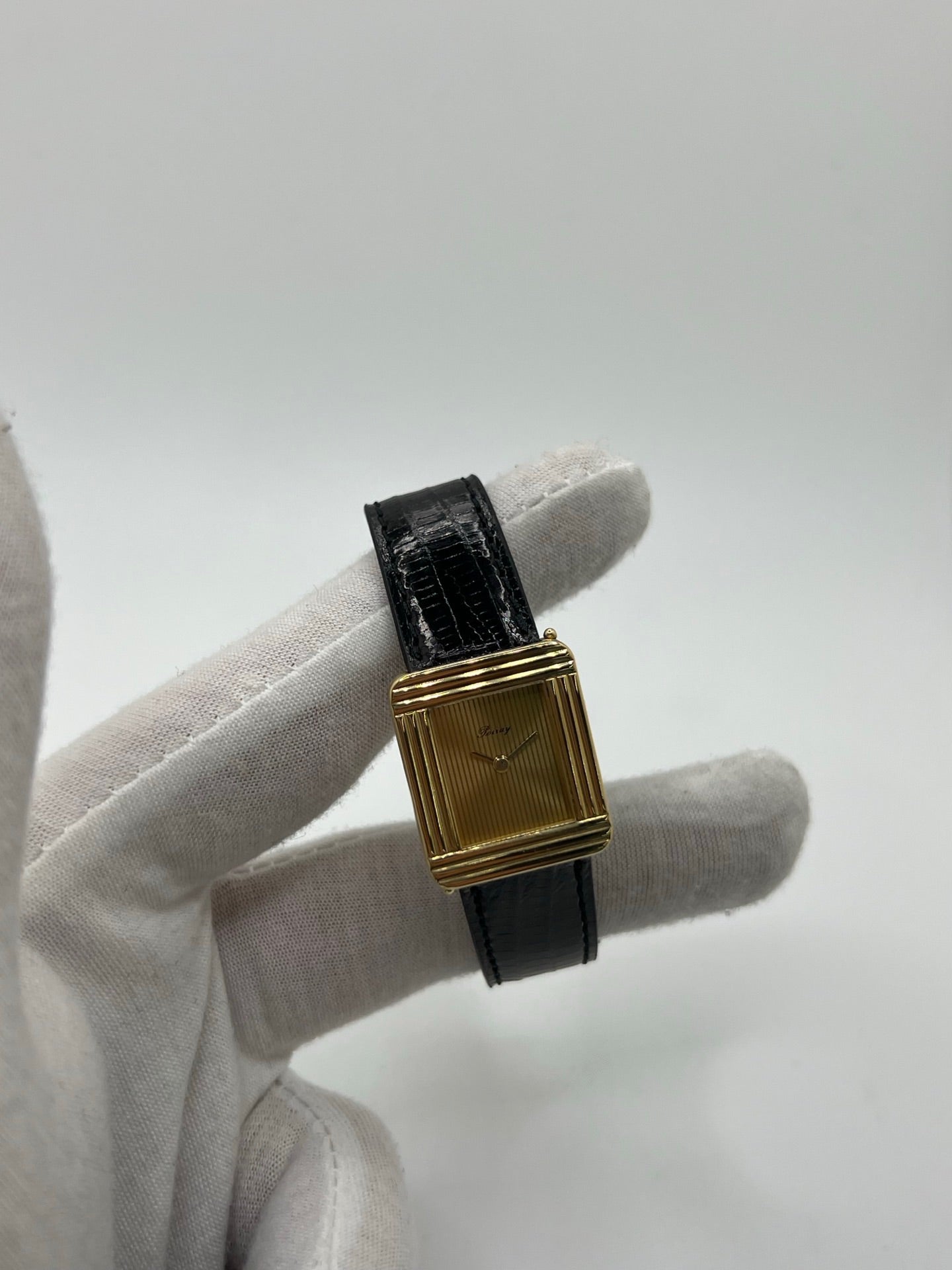 Montre femme Poiray Ma Première en or jaune 18K avec boîtier rectangulaire 22 x 26 mm, cadran doré sans chiffres et verre saphir. Modèle élégant équipé d’un mouvement quartz, bracelet en cuir noir et boucle en acier. Pièce d’occasion en très bon état présentant de légères traces d’usure non perceptibles. Montre raffinée, révisée récemment, idéale pour un style intemporel.