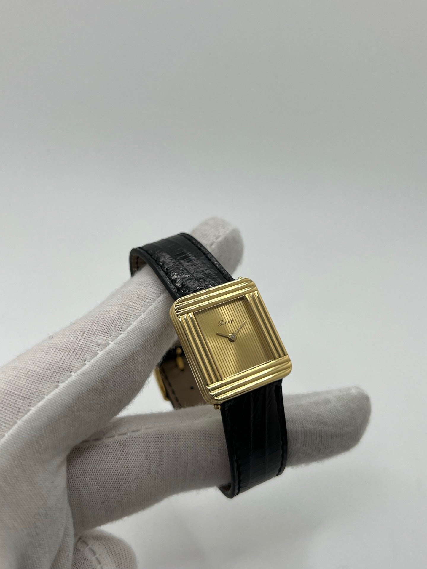 Montre femme Poiray Ma Première en or jaune 18K avec boîtier rectangulaire 22 x 26 mm, cadran doré sans chiffres et verre saphir. Modèle élégant équipé d’un mouvement quartz, bracelet en cuir noir et boucle en acier. Pièce d’occasion en très bon état présentant de légères traces d’usure non perceptibles. Montre raffinée, révisée récemment, idéale pour un style intemporel.