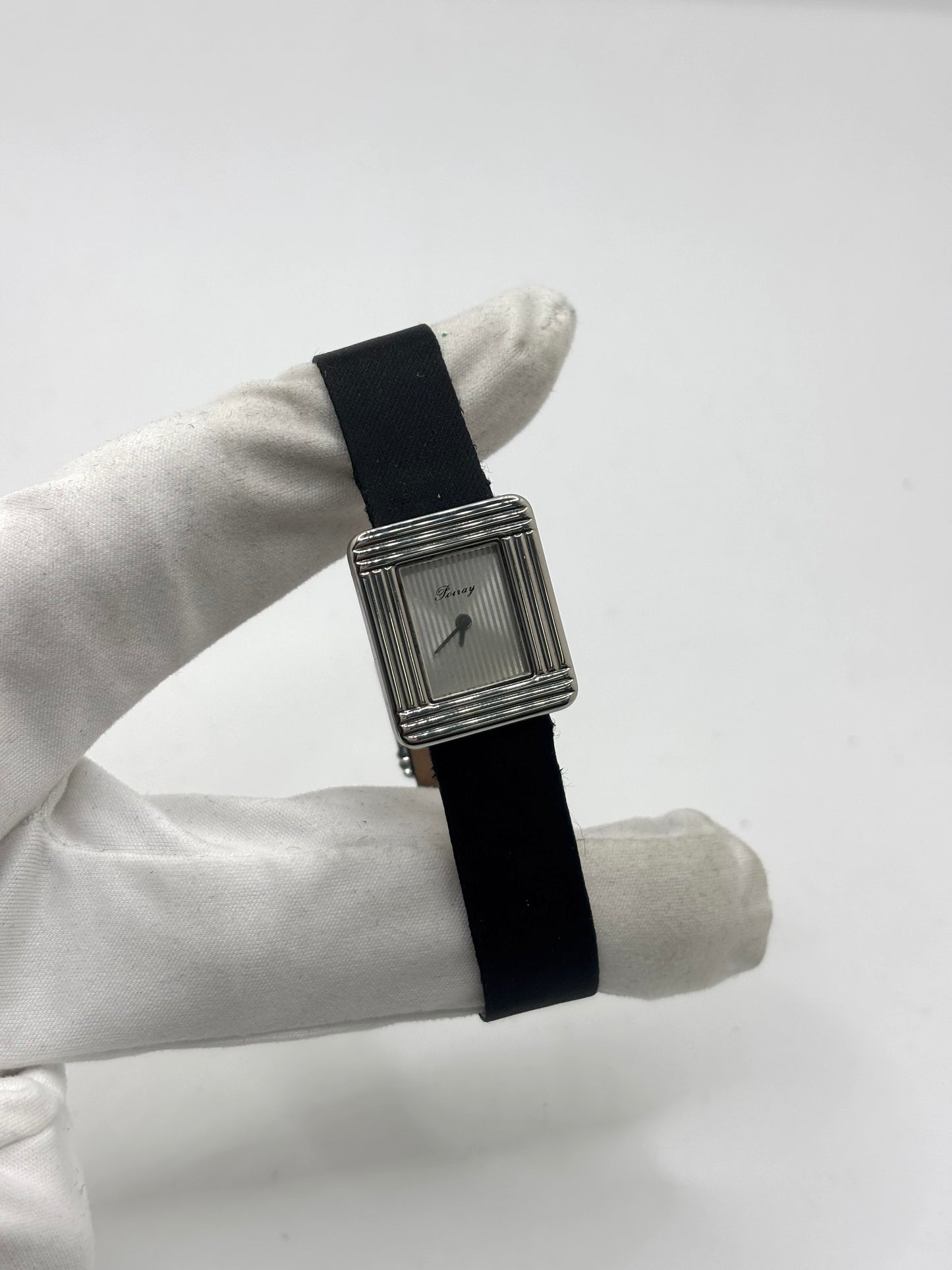 Montre Poiray Ma Première petit modèle en acier avec boîtier de 21,30 × 18,20 mm, cadran blanc épuré sans chiffres et verre minéral. Animée par un mouvement quartz, cette montre femme est équipée de son bracelet textile noir et de sa boucle ardillon d'origine en acier. Révisée, en excellent état et garantie 1 an, cette montre de luxe au style intemporel incarne l'élégance parisienne et le savoir-faire horloger de la maison Poiray.