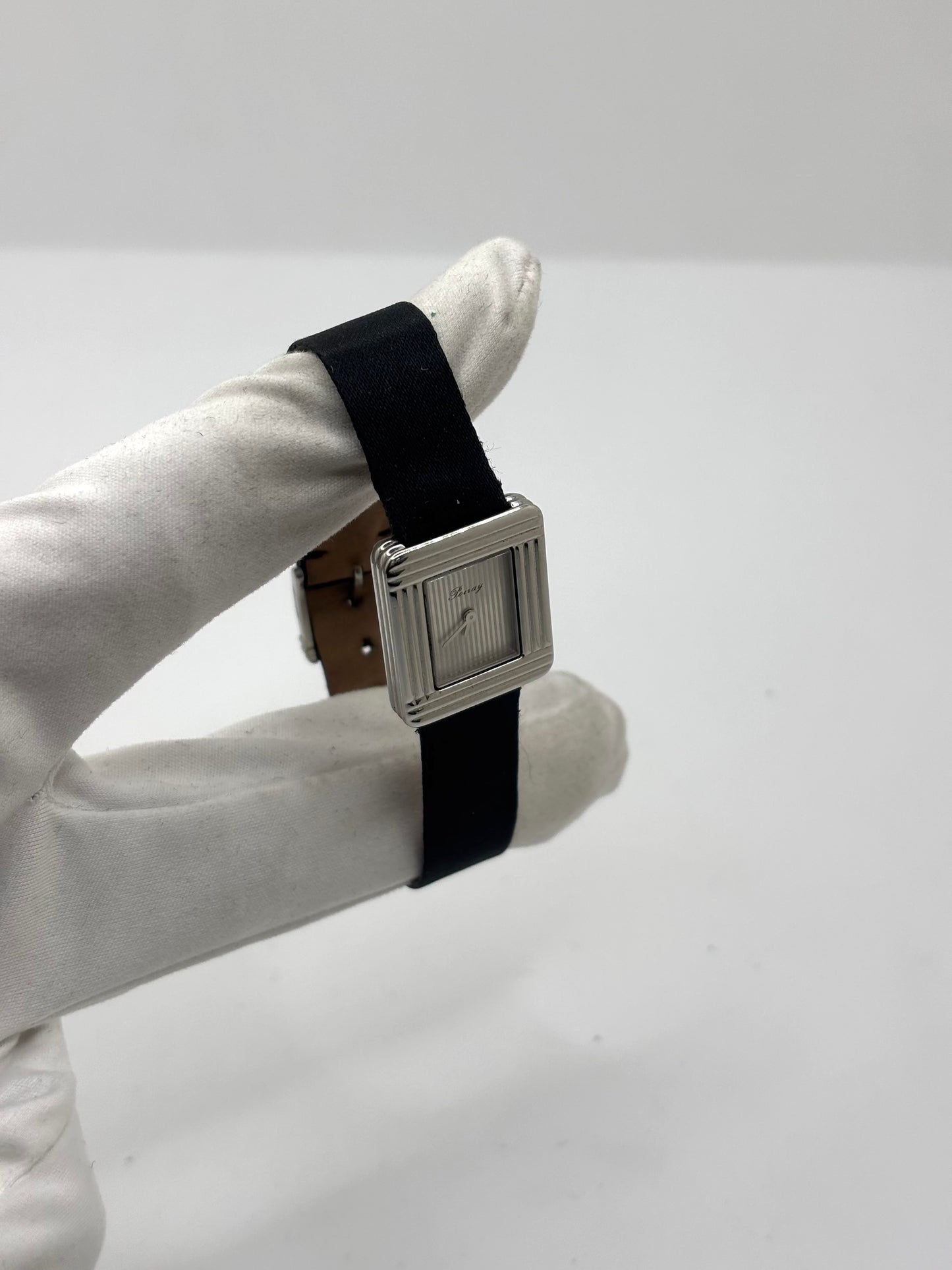 Montre Poiray Ma Première petit modèle en acier avec boîtier de 21,30 × 18,20 mm, cadran blanc épuré sans chiffres et verre minéral. Animée par un mouvement quartz, cette montre femme est équipée de son bracelet textile noir et de sa boucle ardillon d'origine en acier. Révisée, en excellent état et garantie 1 an, cette montre de luxe au style intemporel incarne l'élégance parisienne et le savoir-faire horloger de la maison Poiray.