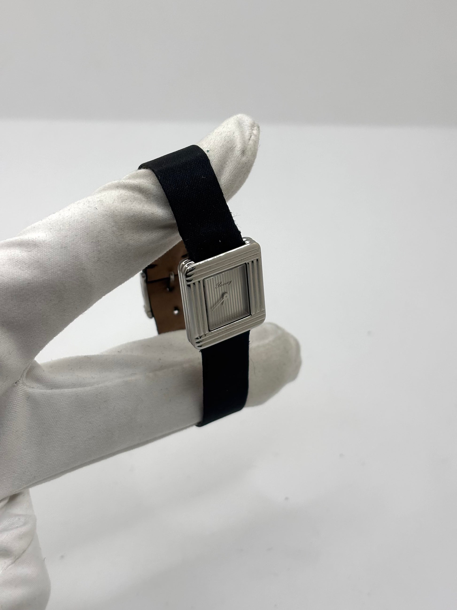 Montre Poiray Ma Première petit modèle en acier avec boîtier de 21,30 × 18,20 mm, cadran blanc épuré sans chiffres et verre minéral. Animée par un mouvement quartz, cette montre femme est équipée de son bracelet textile noir et de sa boucle ardillon d'origine en acier. Révisée, en excellent état et garantie 1 an, cette montre de luxe au style intemporel incarne l'élégance parisienne et le savoir-faire horloger de la maison Poiray.