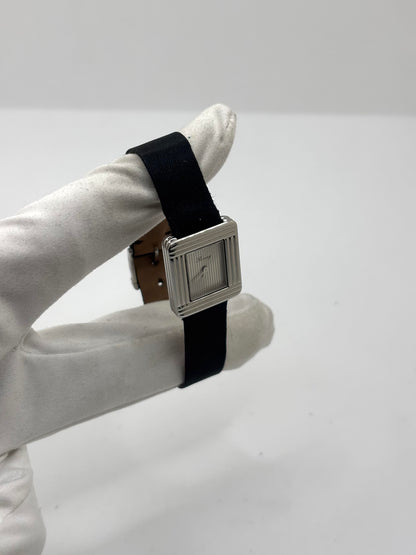 Montre Poiray Ma Première petit modèle en acier avec boîtier de 21,30 × 18,20 mm, cadran blanc épuré sans chiffres et verre minéral. Animée par un mouvement quartz, cette montre femme est équipée de son bracelet textile noir et de sa boucle ardillon d'origine en acier. Révisée, en excellent état et garantie 1 an, cette montre de luxe au style intemporel incarne l'élégance parisienne et le savoir-faire horloger de la maison Poiray.