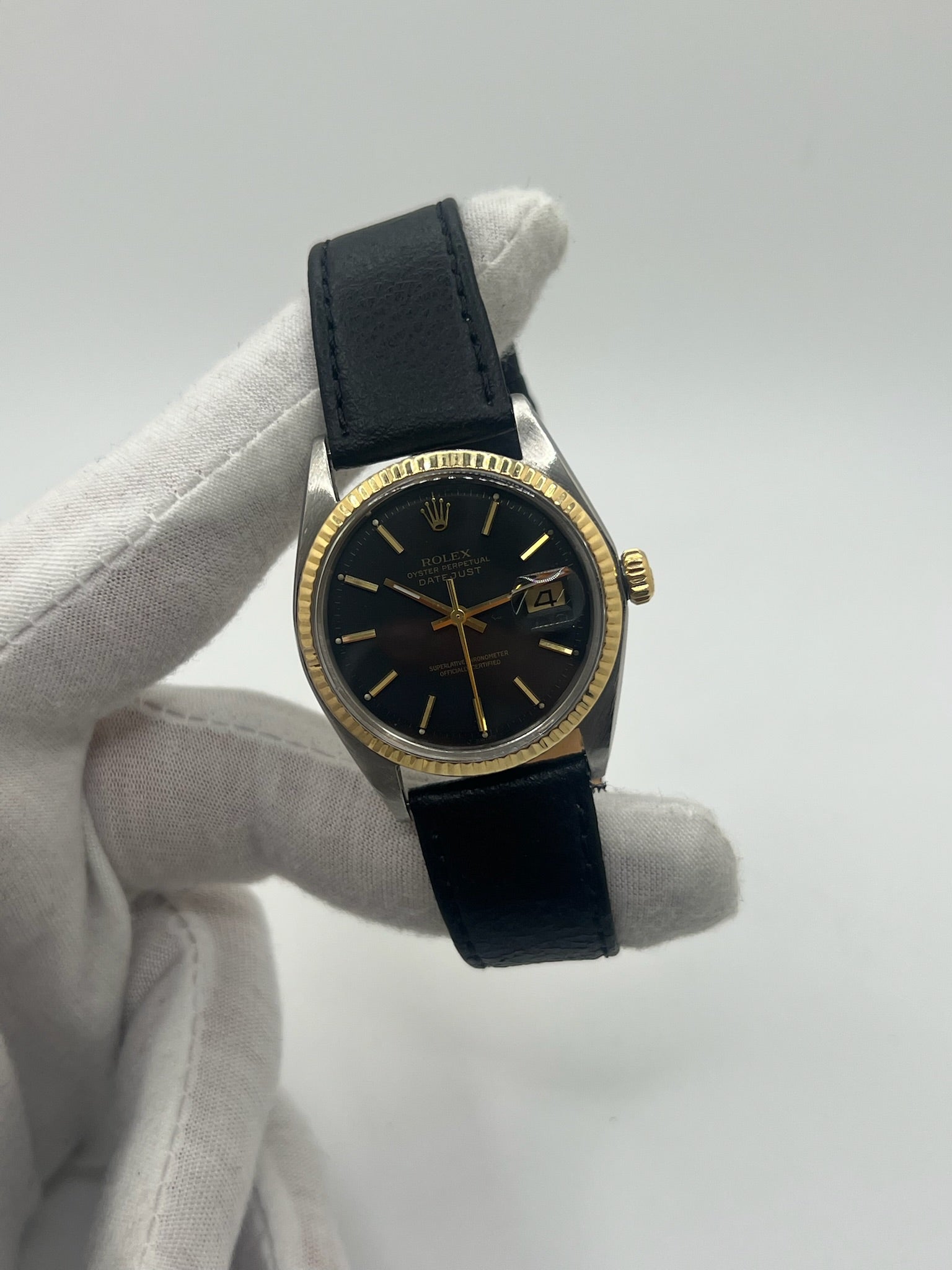Montre Rolex Datejust automatique vintage de 36 mm en acier avec lunette en or jaune, cadran noir épuré sans chiffres et affichage de la date à 3 heures. Boîtier élégant protégé par un verre plexiglas, étanche jusqu’à 10 ATM. Bracelet en cuir noir avec boucle en acier. Mouvement mécanique à remontage automatique offrant environ 40 heures de réserve de marche. Modèle des années 1960, en très bon état, présentant de légères traces d’usure superficielles.