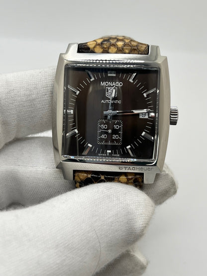 Montre TAG Heuer Monaco Calibre 6 WW2115 pour homme, équipée d’un mouvement automatique offrant une réserve de marche de 42 heures et du calibre 6 doté de 27 pierres. Son boîtier en acier de 37 mm accueille un cadran brun au style élégant et distinctif. Cette TAG Heuer Monaco est montée sur un bracelet en cuir de serpent avec boucle déployante en acier. Dotée d’un affichage de la date, elle allie design emblématique et savoir-faire horloger. Vendue avec son coffret d’origine, en très bon état.
