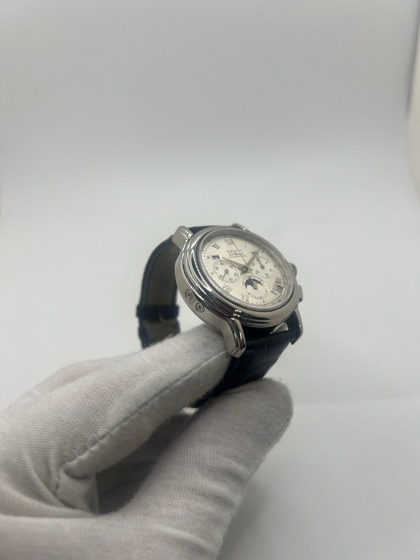 Montre chronographe automatique en acier avec cadran argenté à chiffres romains, fonction phase lunaire, date, jour et mois. Boîtier de 40 mm, verre saphir, fond transparent et bracelet en cuir noir. Modèle de haute précision doté du calibre 410 avec 50 heures de réserve de marche. Montre élégante pour homme ou unisexe.