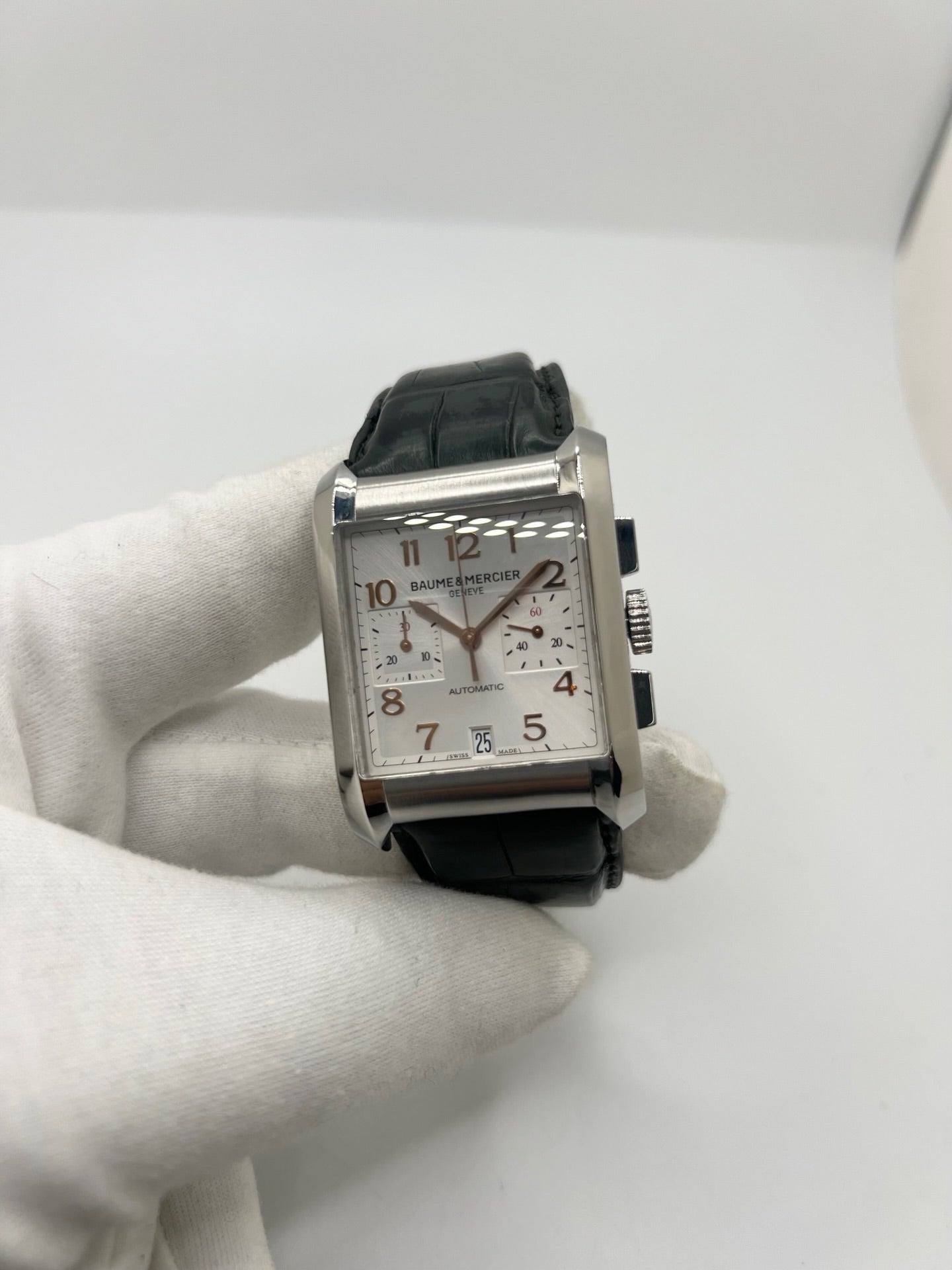 Montre Baume & Mercier Hampton réf. 65698, modèle automatique pour homme ou unisexe. Boîtier en acier de 34,5 mm avec verre saphir résistant aux rayures. Cadran argent avec index en chiffres arabes, offrant une lecture élégante et classique. Bracelet en cuir vert avec boucle déployante en acier. Fonction chronographe et date. Montre de luxe d’occasion en très bon état, avec légères traces d’usure. Révisée le 24 juin 2026 en interne. Livrée sans coffret ni papiers. Disponible à Paris.