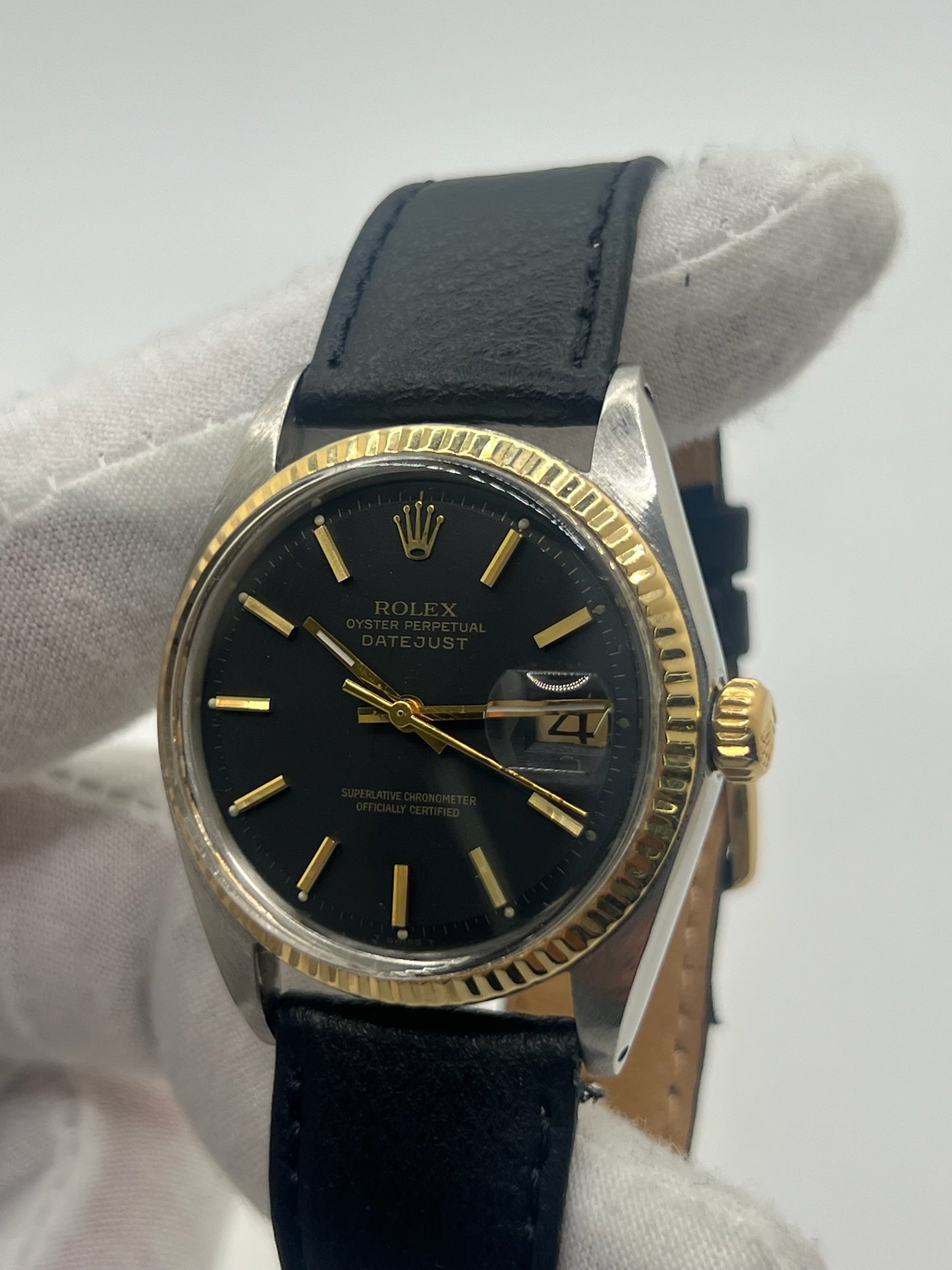 Montre Rolex Datejust automatique vintage de 36 mm en acier avec lunette en or jaune, cadran noir épuré sans chiffres et affichage de la date à 3 heures. Boîtier élégant protégé par un verre plexiglas, étanche jusqu’à 10 ATM. Bracelet en cuir noir avec boucle en acier. Mouvement mécanique à remontage automatique offrant environ 40 heures de réserve de marche. Modèle des années 1960, en très bon état, présentant de légères traces d’usure superficielles.