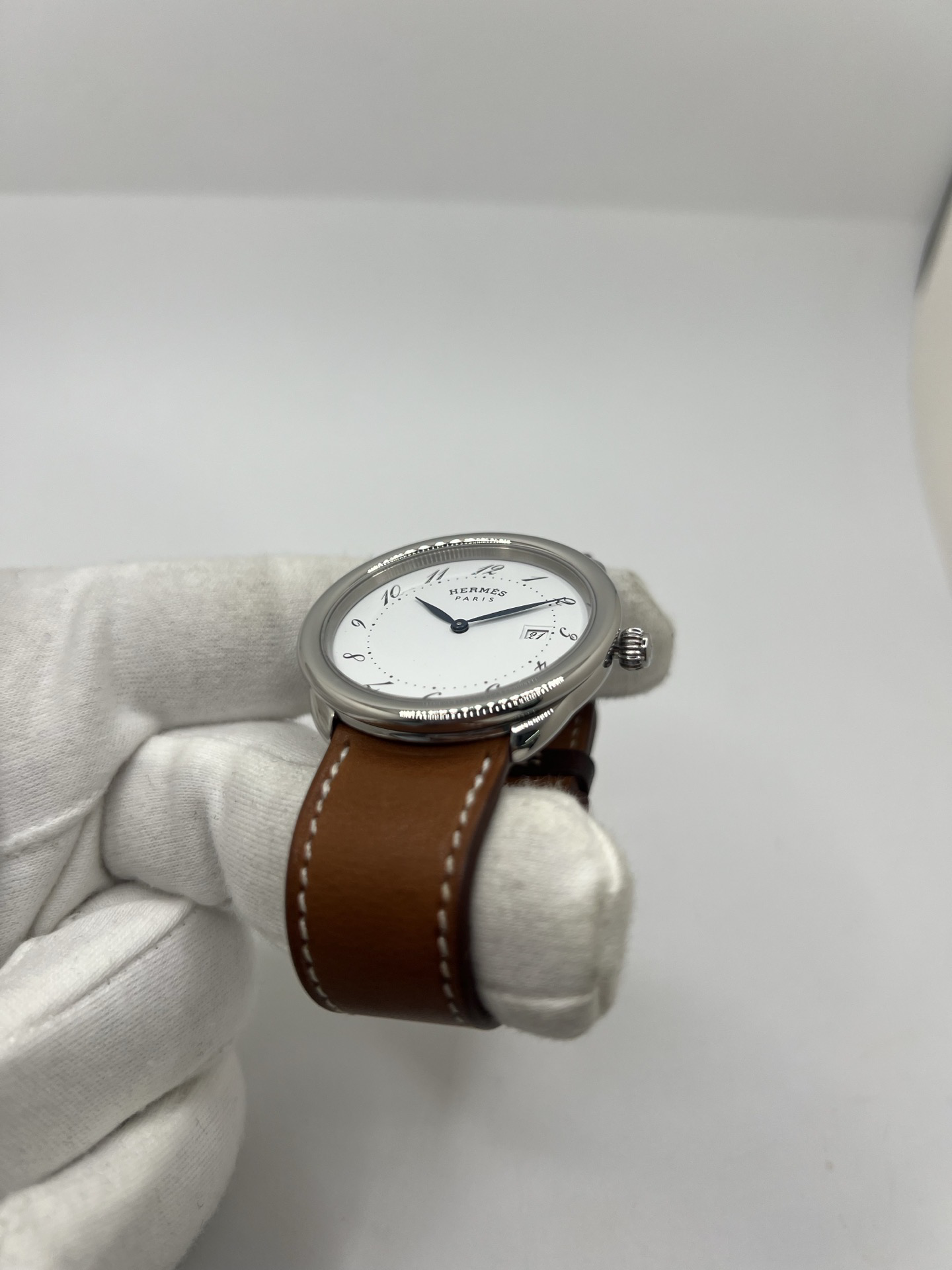 Montre Hermès Arceau Grand Modèle AR5.710 de 2014 en acier 38 mm avec mouvement quartz, cadran blanc à chiffres arabes et bracelet cuir brun d’origine. Cette montre de luxe Hermès Full Set avec boîte et papiers possède un verre saphir, une boucle ardillon acier et le design emblématique Arceau inspiré de l’univers équestre. Montre vintage Hermès élégante, révisée en 2026 et garantie 1 an.