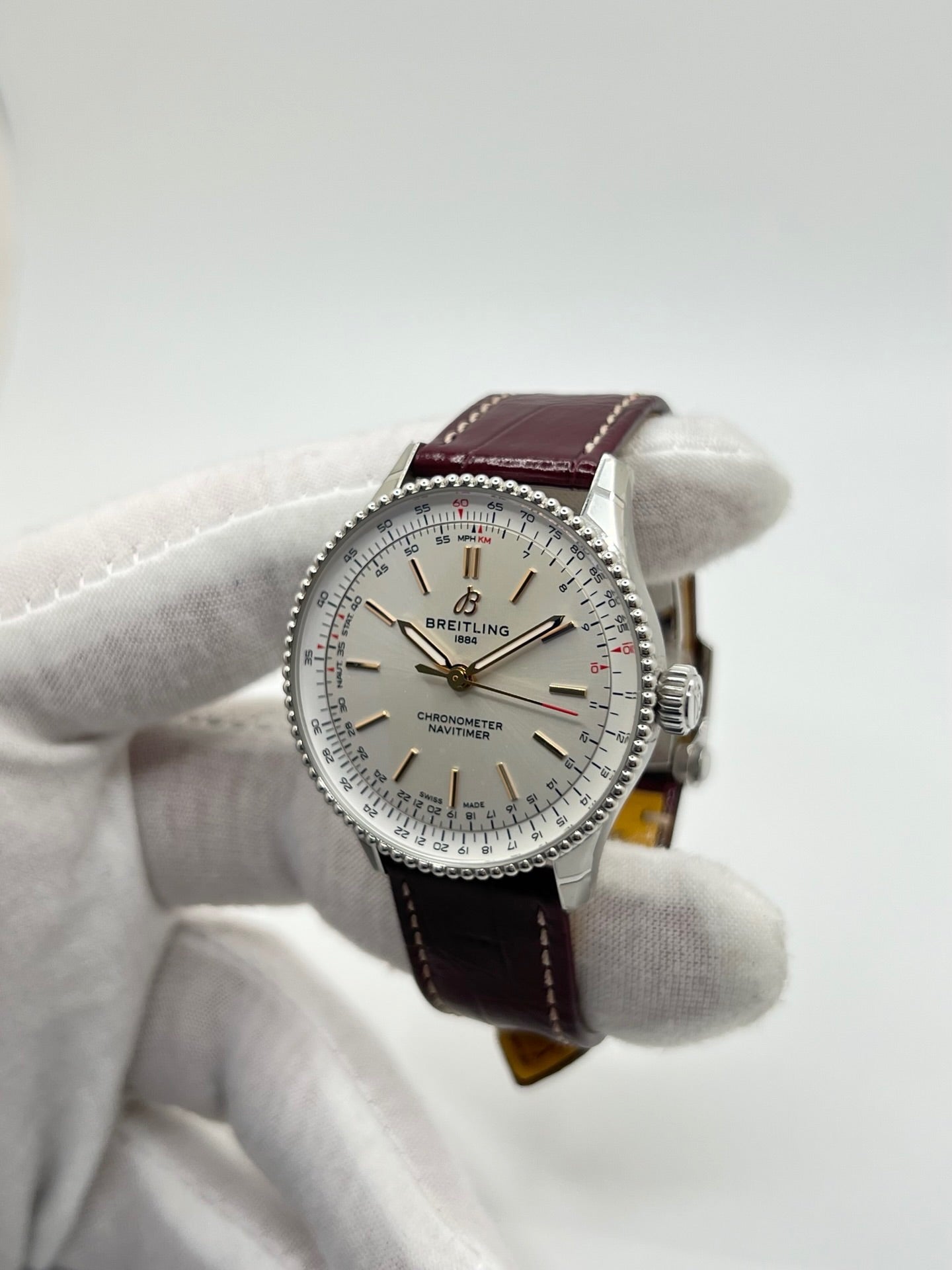 Montre Breitling Navitimer A17327211G1P1 pour femme, modèle automatique en acier de 36 mm avec cadran argent sans chiffres et verre saphir. Cette montre de luxe dispose du calibre Breitling 17 avec une réserve de marche de 38 heures. Elle est équipée d’un bracelet en cuir bordeaux avec boucle déployante en acier. Montre étanche à 3 ATM, état neuf, jamais portée, sans coffret ni papiers d’origine.