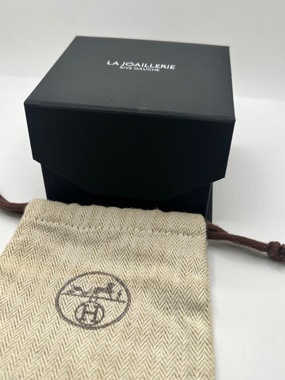 Montre Hermès Heure H HH1.201 pour femme, équipée d’un mouvement quartz et d’un boîtier en acier de 21 mm. Son cadran couleur or est protégé par un verre saphir et accompagné d’un bracelet brun en cuir de vache avec boucle ardillon en acier. Étanche à 3 ATM, cette montre Hermès Heure H se distingue par son célèbre boîtier en forme de H et son design élégant. En très bon état, elle présente de légères traces d’usure.
