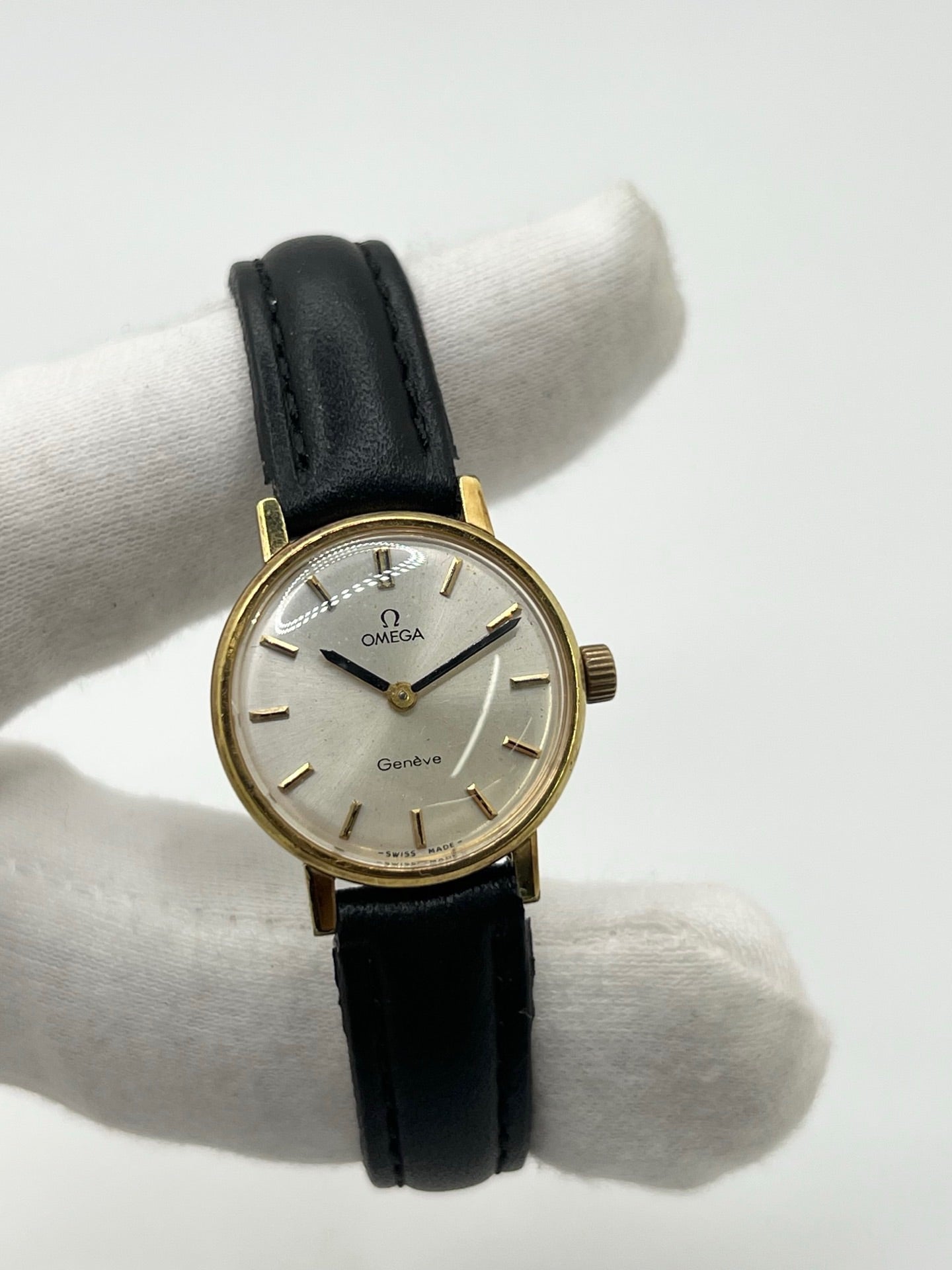 Montre Omega Genève femme vintage de 1972 en plaqué or, avec mouvement à remontage manuel. Boîtier de 23 mm au cadran doré orné de pierres précieuses et verre en plastique. Bracelet en cuir noir avec boucle en acier. Modèle élégant et intemporel, en bon état avec traces d’usure visibles. Révisée en avril 2026, vendue sans coffret ni papiers, disponible en stock en France.