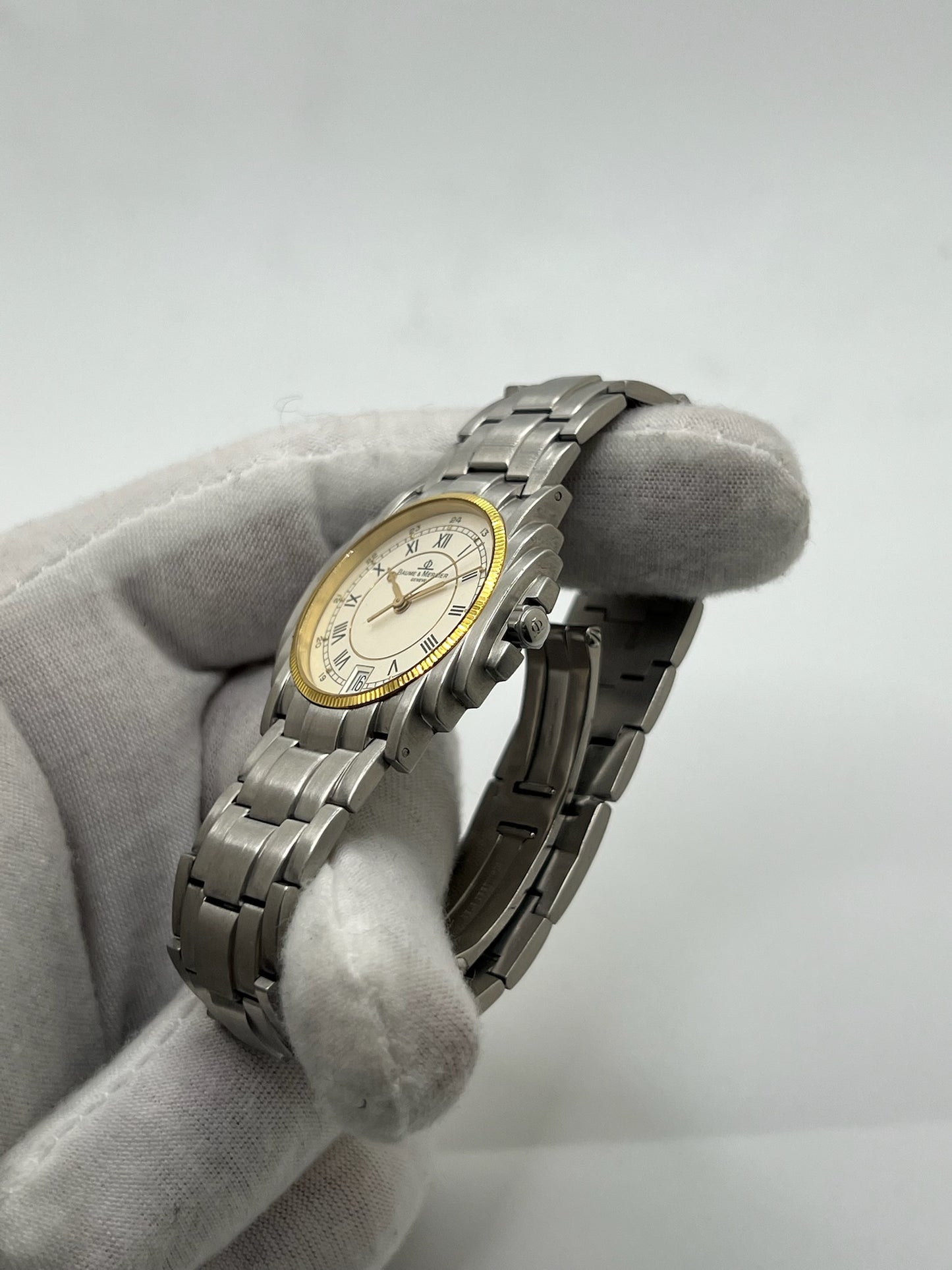 Montre Baume & Mercier 5136.018.3 pour homme/unisexe, boîtier 34 mm en or et acier, cadran blanc à chiffres romains, mouvement quartz précis. Verre saphir résistant aux rayures, bracelet en acier avec boucle double plis. Fonction date. Montre d’occasion en très bon état avec papiers d’origine, élégante et intemporelle.