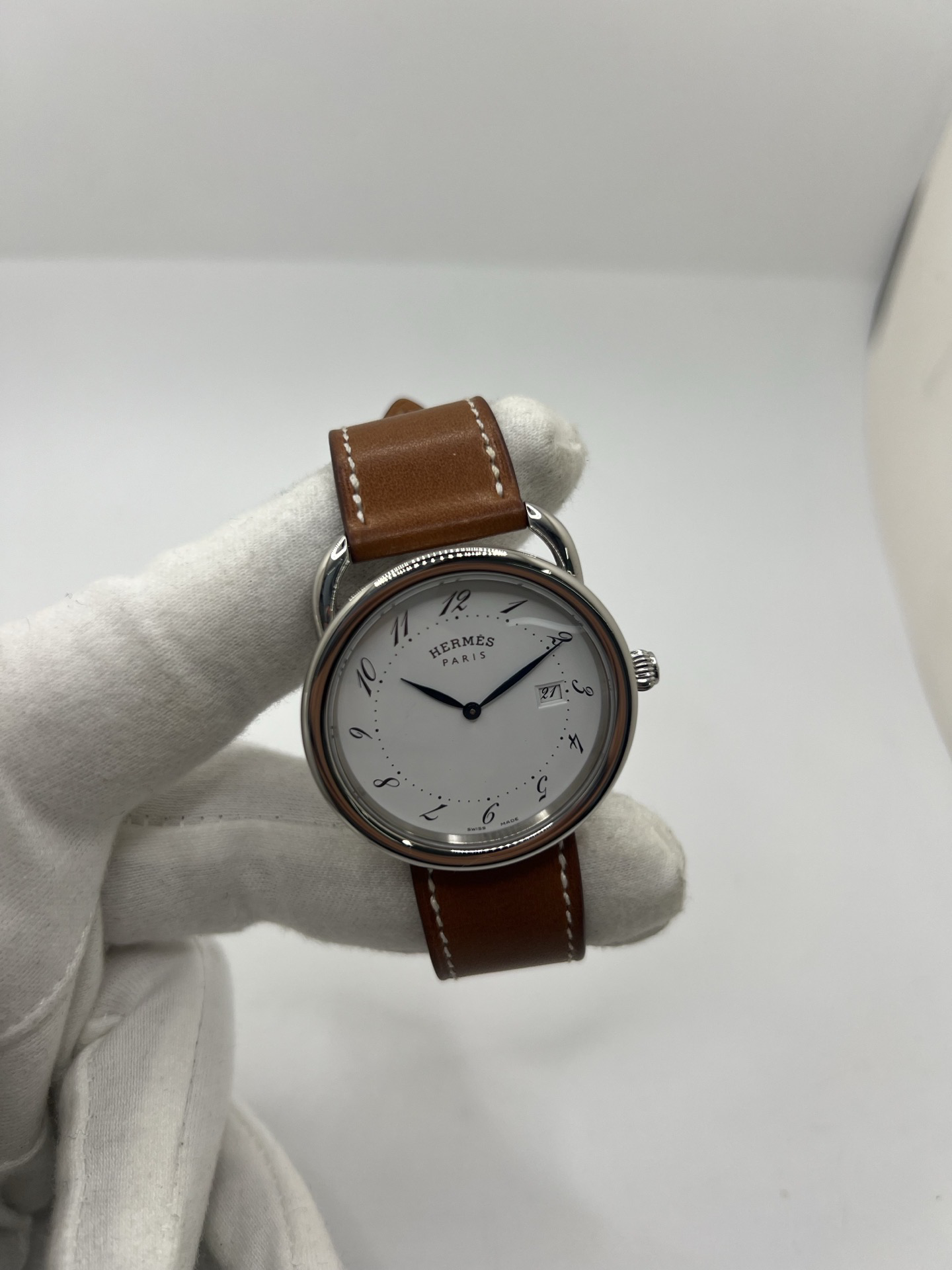 Montre Hermès Arceau Grand Modèle AR5.710 de 2014 en acier 38 mm avec mouvement quartz, cadran blanc à chiffres arabes et bracelet cuir brun d’origine. Cette montre de luxe Hermès Full Set avec boîte et papiers possède un verre saphir, une boucle ardillon acier et le design emblématique Arceau inspiré de l’univers équestre. Montre vintage Hermès élégante, révisée en 2026 et garantie 1 an.