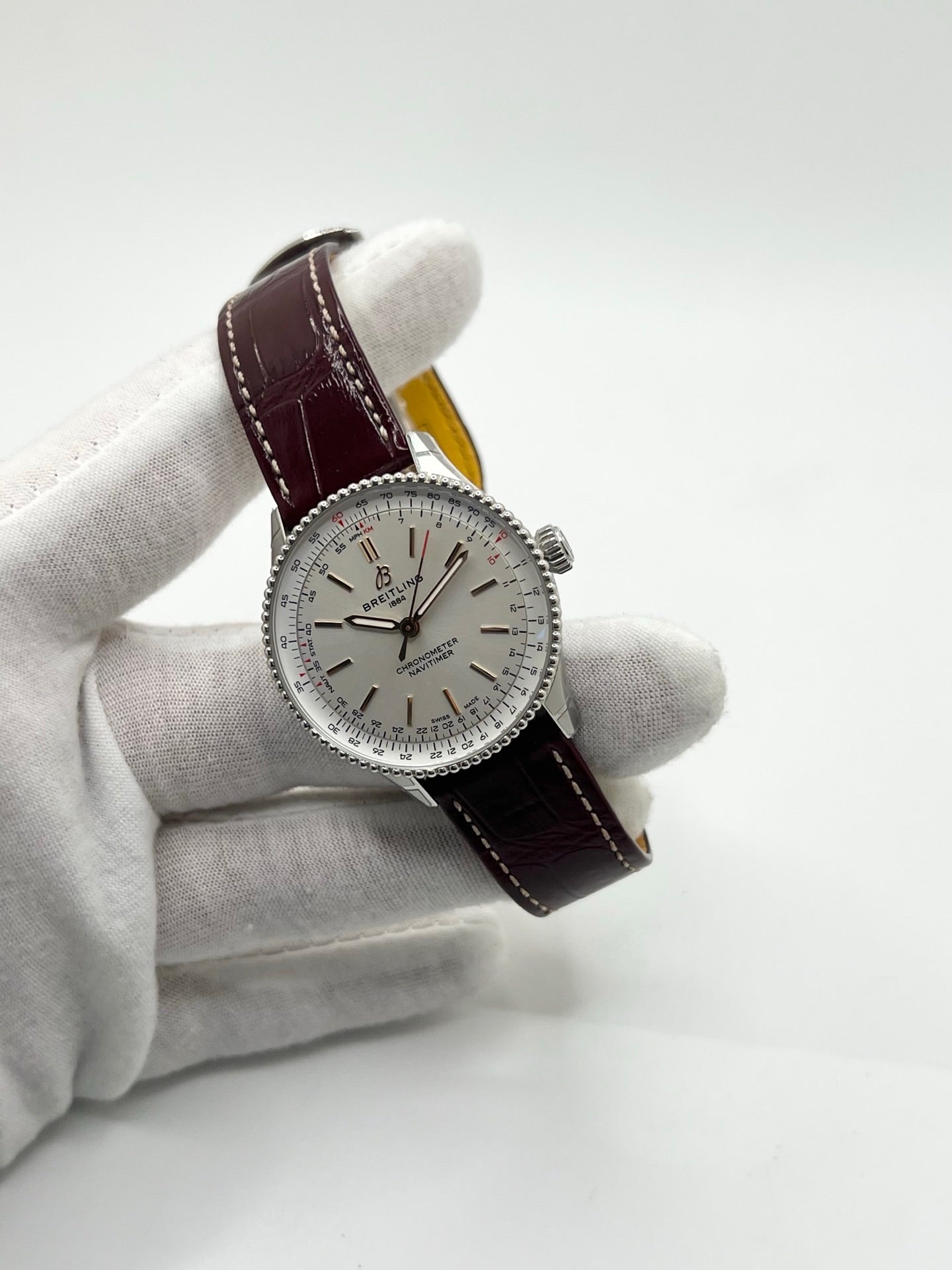 Montre Breitling Navitimer A17327211G1P1 pour femme, modèle automatique en acier de 36 mm avec cadran argent sans chiffres et verre saphir. Cette montre de luxe dispose du calibre Breitling 17 avec une réserve de marche de 38 heures. Elle est équipée d’un bracelet en cuir bordeaux avec boucle déployante en acier. Montre étanche à 3 ATM, état neuf, jamais portée, sans coffret ni papiers d’origine.