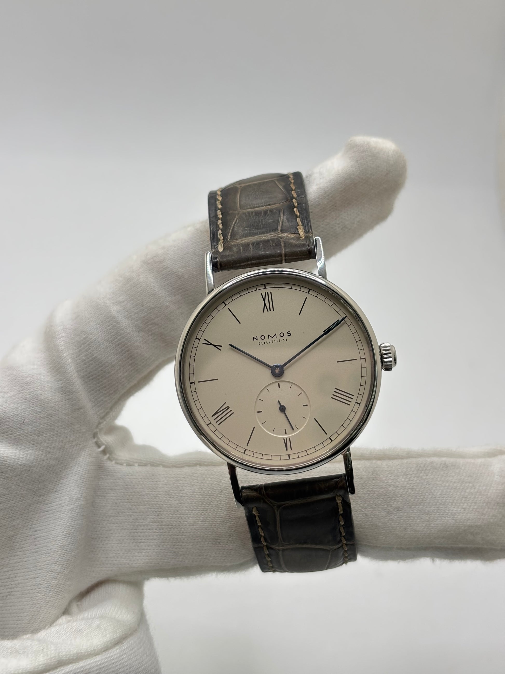 Montre Nomos Glashütte Ludwig 205 en acier avec boîtier de 37,5 mm, mouvement à remontage manuel offrant 43 heures de réserve de marche et cadran blanc à chiffres romains. Équipée d'un verre saphir, d'un bracelet en cuir noir, d'une petite seconde, d'un fond transparent et d'aiguilles en acier bleui, cette montre de luxe d'occasion est en très bon état avec de légères traces d'usure. Un modèle élégant au style intemporel, idéal pour les amateurs d'horlogerie.

