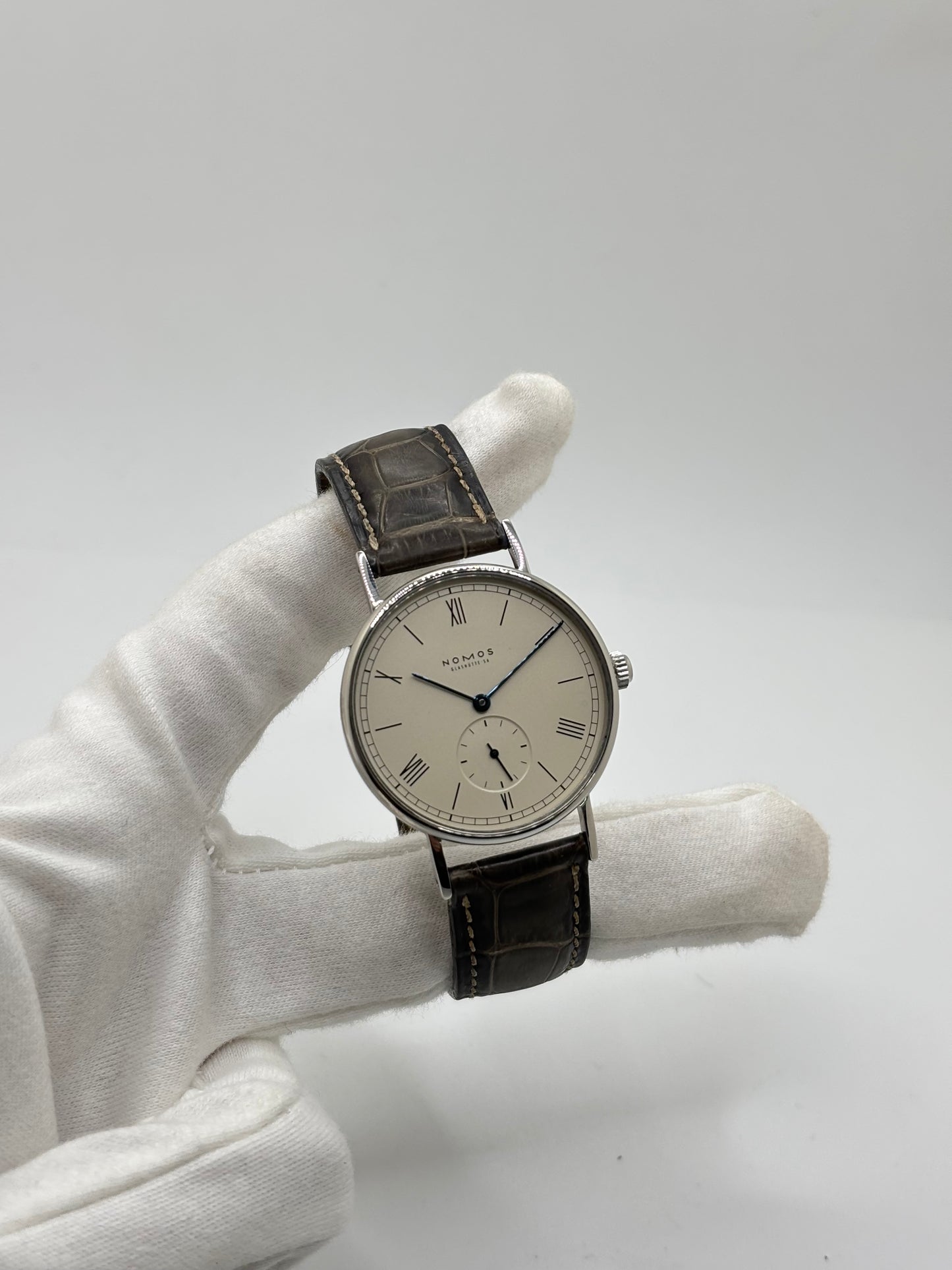 Montre Nomos Glashütte Ludwig 205 en acier avec boîtier de 37,5 mm, mouvement à remontage manuel offrant 43 heures de réserve de marche et cadran blanc à chiffres romains. Équipée d'un verre saphir, d'un bracelet en cuir noir, d'une petite seconde, d'un fond transparent et d'aiguilles en acier bleui, cette montre de luxe d'occasion est en très bon état avec de légères traces d'usure. Un modèle élégant au style intemporel, idéal pour les amateurs d'horlogerie.
