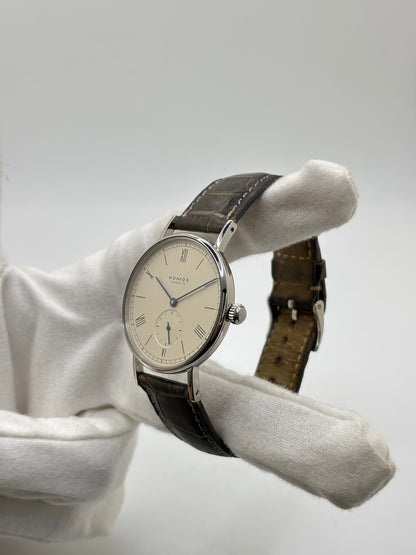 Montre Nomos Glashütte Ludwig 205 en acier avec boîtier de 37,5 mm, mouvement à remontage manuel offrant 43 heures de réserve de marche et cadran blanc à chiffres romains. Équipée d'un verre saphir, d'un bracelet en cuir noir, d'une petite seconde, d'un fond transparent et d'aiguilles en acier bleui, cette montre de luxe d'occasion est en très bon état avec de légères traces d'usure. Un modèle élégant au style intemporel, idéal pour les amateurs d'horlogerie.
