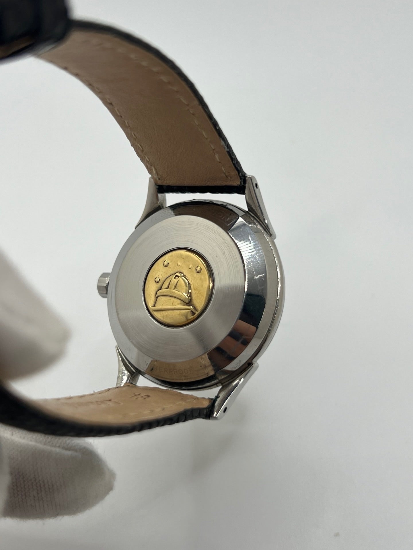 Montre automatique vintage en acier avec boîtier rond de 35 mm, cadran noir à chiffres arabes et verre plexiglas. Modèle chronomètre des années 1950 équipé d’un calibre automatique 505 avec réserve de marche de 46 heures. Bracelet en cuir noir avec boucle ardillon en acier. Montre d’occasion présentant des traces d’usure visibles, révisée récemment, sans coffret ni papiers d’origine.