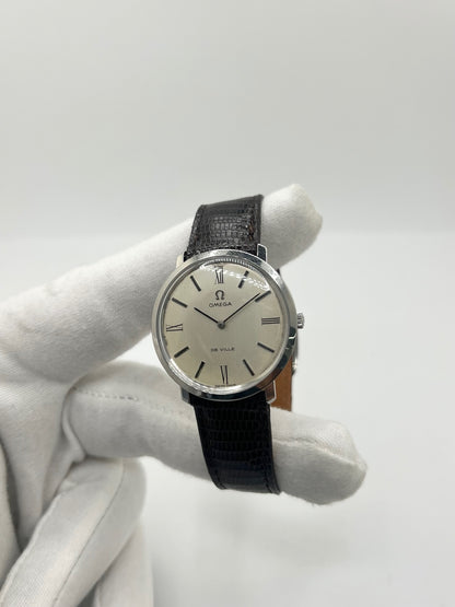 Montre Omega De Ville vintage référence 111.077 en acier, fabriquée en 1969. Ce modèle à remontage manuel est doté d'un cadran argent avec chiffres romains, d'un verre en plexiglas et d'un boîtier de 33 mm. Le bracelet en cuir noir avec boucle ardillon en acier complète son style classique et intemporel. Cette montre d'occasion révisée séduit les amateurs d'horlogerie vintage et de montres Omega de collection.
