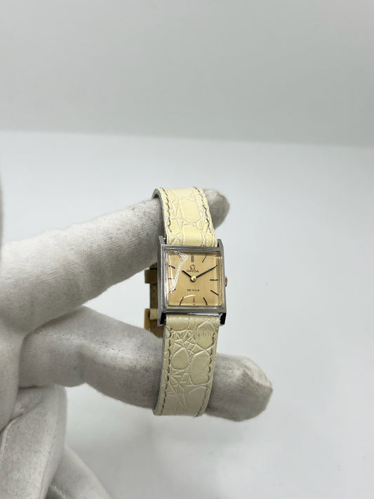 Montre Omega De Ville 511.087 vintage pour femme en acier, fabriquée en 1966. Cette montre élégante est dotée d'un cadran champagne avec index bâtons, d'un mouvement à remontage manuel calibre 620 et d'un verre en plexiglas. Elle est montée sur un bracelet en cuir beige avec boucle ardillon en acier. Son format de 19,5 mm lui confère une allure raffinée et intemporelle. Montre de collection en très bon état d'occasion, révisée et prête à être portée.