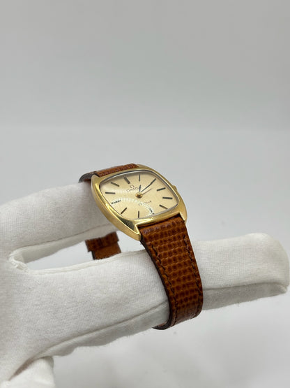 Montre Omega De Ville vintage référence 511.0531 en plaqué or datant de 1969, équipée d'un mouvement à remontage manuel. Son cadran doré à index bâtons est protégé par un verre en matière plastique. Son boîtier de 25 mm est associé à un bracelet en cuir brun avec boucle ardillon en acier. Cette montre d'occasion, révisée et en très bon état, séduit par son élégance intemporelle et son style classique des années 1960.