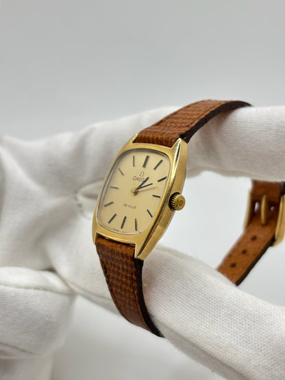 Montre Omega De Ville vintage référence 511.0531 en plaqué or datant de 1969, équipée d'un mouvement à remontage manuel. Son cadran doré à index bâtons est protégé par un verre en matière plastique. Son boîtier de 25 mm est associé à un bracelet en cuir brun avec boucle ardillon en acier. Cette montre d'occasion, révisée et en très bon état, séduit par son élégance intemporelle et son style classique des années 1960.