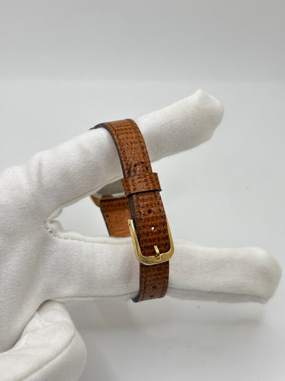 Montre Omega De Ville vintage référence 511.0531 en plaqué or datant de 1969, équipée d'un mouvement à remontage manuel. Son cadran doré à index bâtons est protégé par un verre en matière plastique. Son boîtier de 25 mm est associé à un bracelet en cuir brun avec boucle ardillon en acier. Cette montre d'occasion, révisée et en très bon état, séduit par son élégance intemporelle et son style classique des années 1960.