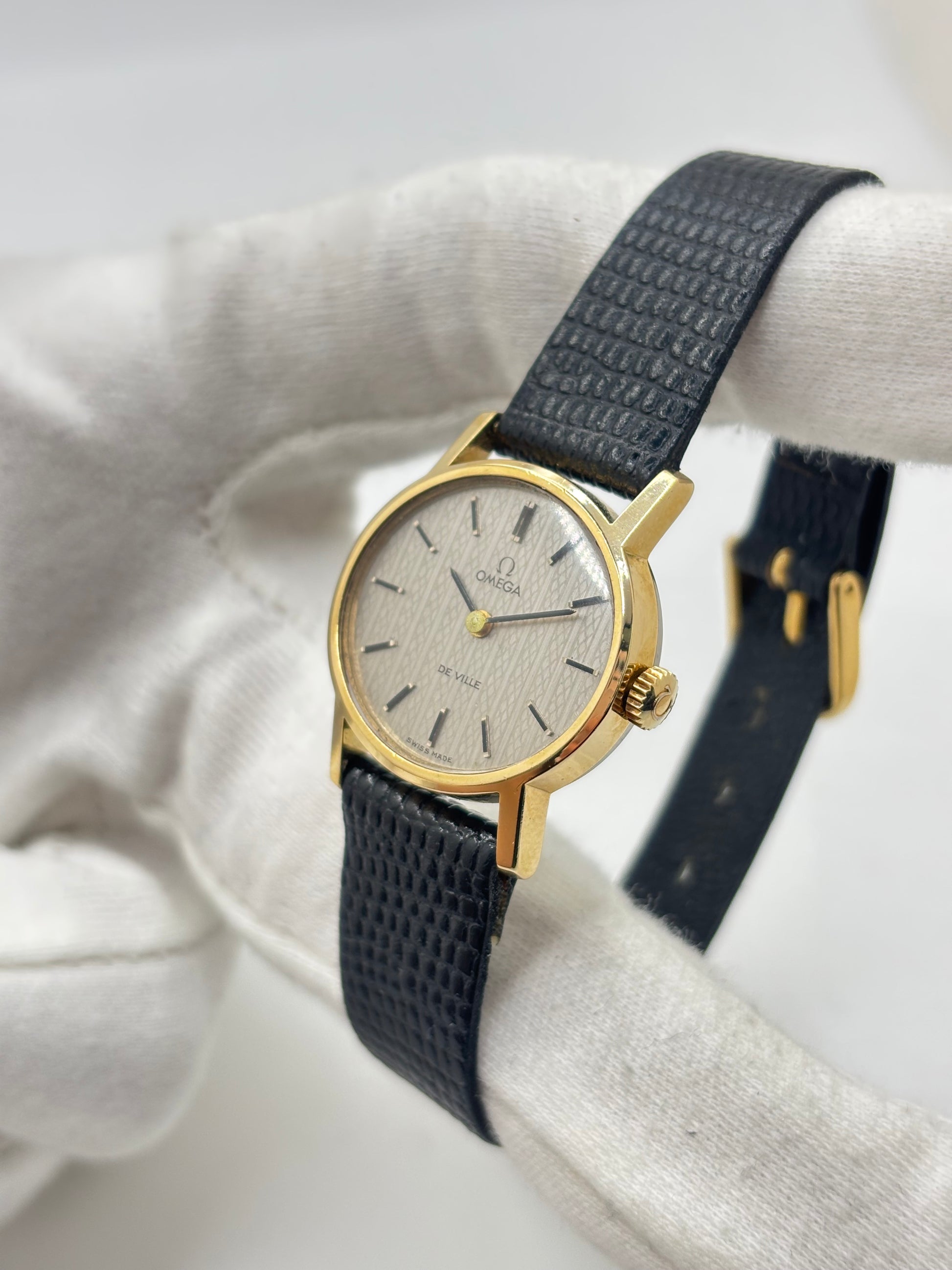 Montre Omega De Ville vintage référence 511.0508 pour femme, datant de 1967, avec boîtier en acier de 24 mm et cadran gris à index bâtons. Cette montre à remontage manuel est équipée du calibre Omega 625 à 17 rubis et est montée sur un bracelet en cuir noir avec boucle ardillon en acier. Révisée et en très bon état, elle présente de légères traces d'usure conformes à son âge. Une montre de collection au design élégant, idéale pour les amateurs d'horlogerie vintage.