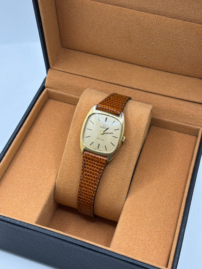 Montre Omega De Ville vintage référence 511.0531 en plaqué or datant de 1969, équipée d'un mouvement à remontage manuel. Son cadran doré à index bâtons est protégé par un verre en matière plastique. Son boîtier de 25 mm est associé à un bracelet en cuir brun avec boucle ardillon en acier. Cette montre d'occasion, révisée et en très bon état, séduit par son élégance intemporelle et son style classique des années 1960.