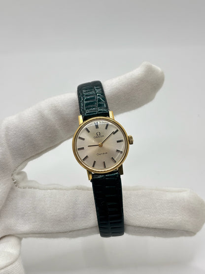 Montre Omega Genève vintage référence 511.0457 pour femme, fabriquée vers 1972 et équipée d'un mouvement à remontage manuel. Son boîtier en acier de 23 mm est associé à un cadran blanc à index bâtons protégé par un verre en matière plastique. Elle est montée sur un bracelet en cuir vert avec boucle ardillon en acier. Révisée en interne et proposée en très bon état, cette montre d'occasion incarne l'élégance discrète et le savoir-faire horloger suisse des années 1970.