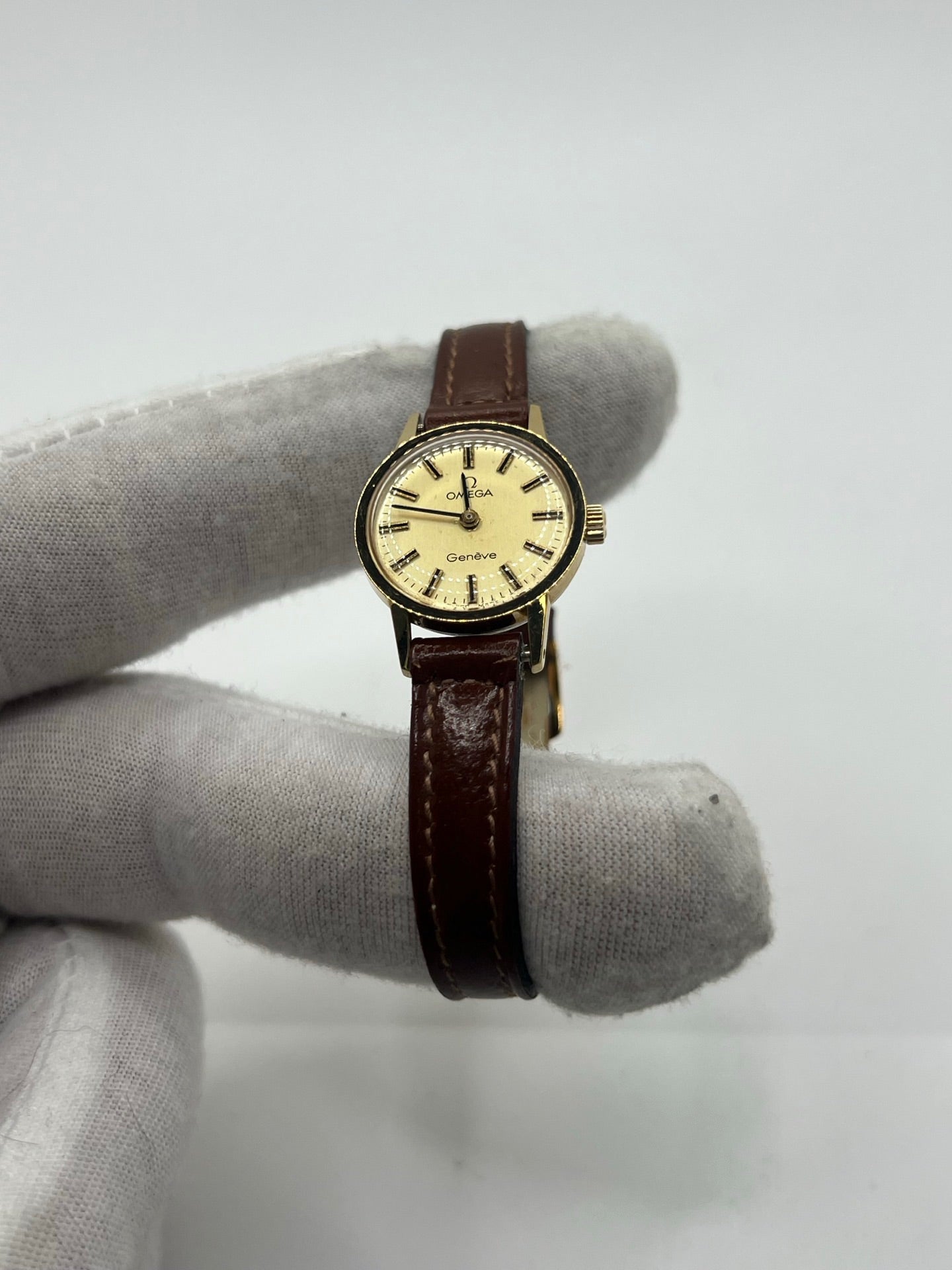 Montre Omega Genève Lady en acier avec boîtier plaqué or de 20 mm, cadran or à index bâtons, mouvement calibre 560, bracelet en cuir brun avec boucle acier. Vintage de 1978, d'occasion en bon état avec traces d'usure visibles. Verre plexiglas, modèle élégant pour femme, idéal pour collection ou usage quotidien. Livrée sans coffret ni papiers d'origine, disponible en stock à Paris.