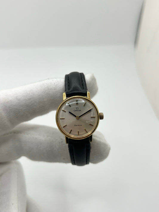Montre Omega Genève femme vintage de 1972 en plaqué or, avec mouvement à remontage manuel. Boîtier de 23 mm au cadran doré orné de pierres précieuses et verre en plastique. Bracelet en cuir noir avec boucle en acier. Modèle élégant et intemporel, en bon état avec traces d’usure visibles. Révisée en avril 2026, vendue sans coffret ni papiers, disponible en stock en France.