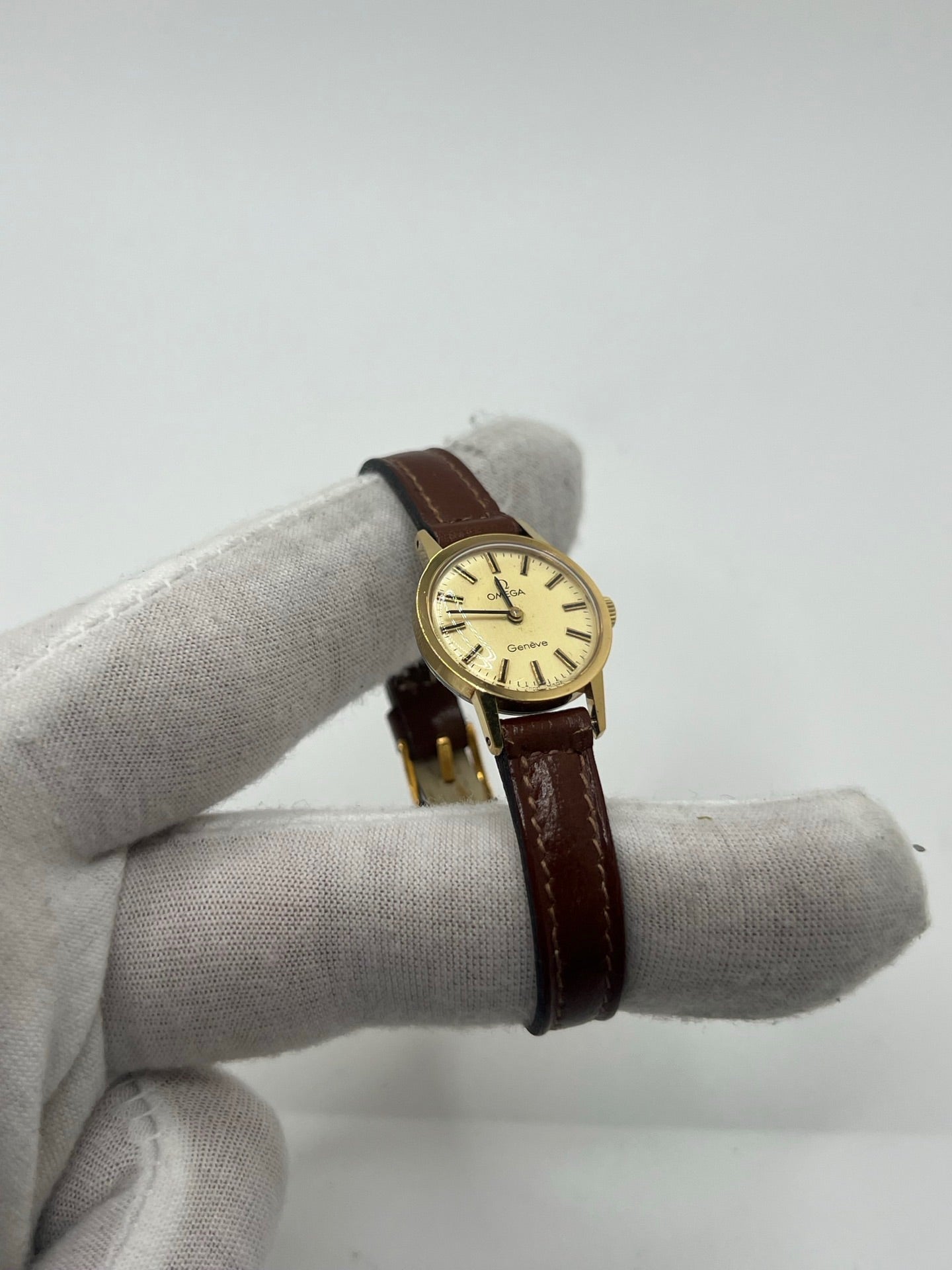 Montre Omega Genève Lady en acier avec boîtier plaqué or de 20 mm, cadran or à index bâtons, mouvement calibre 560, bracelet en cuir brun avec boucle acier. Vintage de 1978, d'occasion en bon état avec traces d'usure visibles. Verre plexiglas, modèle élégant pour femme, idéal pour collection ou usage quotidien. Livrée sans coffret ni papiers d'origine, disponible en stock à Paris.