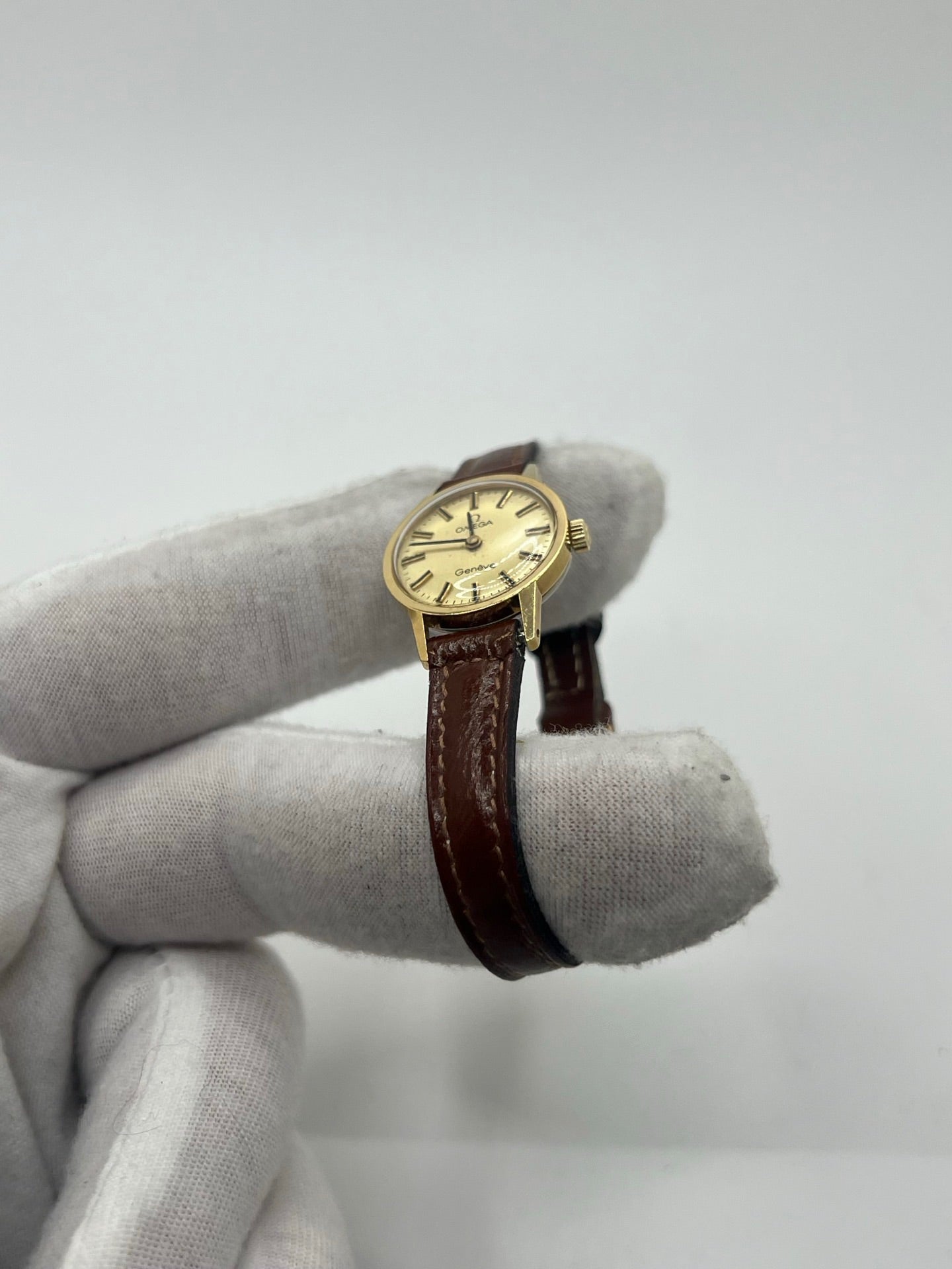 Montre Omega Genève Lady en acier avec boîtier plaqué or de 20 mm, cadran or à index bâtons, mouvement calibre 560, bracelet en cuir brun avec boucle acier. Vintage de 1978, d'occasion en bon état avec traces d'usure visibles. Verre plexiglas, modèle élégant pour femme, idéal pour collection ou usage quotidien. Livrée sans coffret ni papiers d'origine, disponible en stock à Paris.